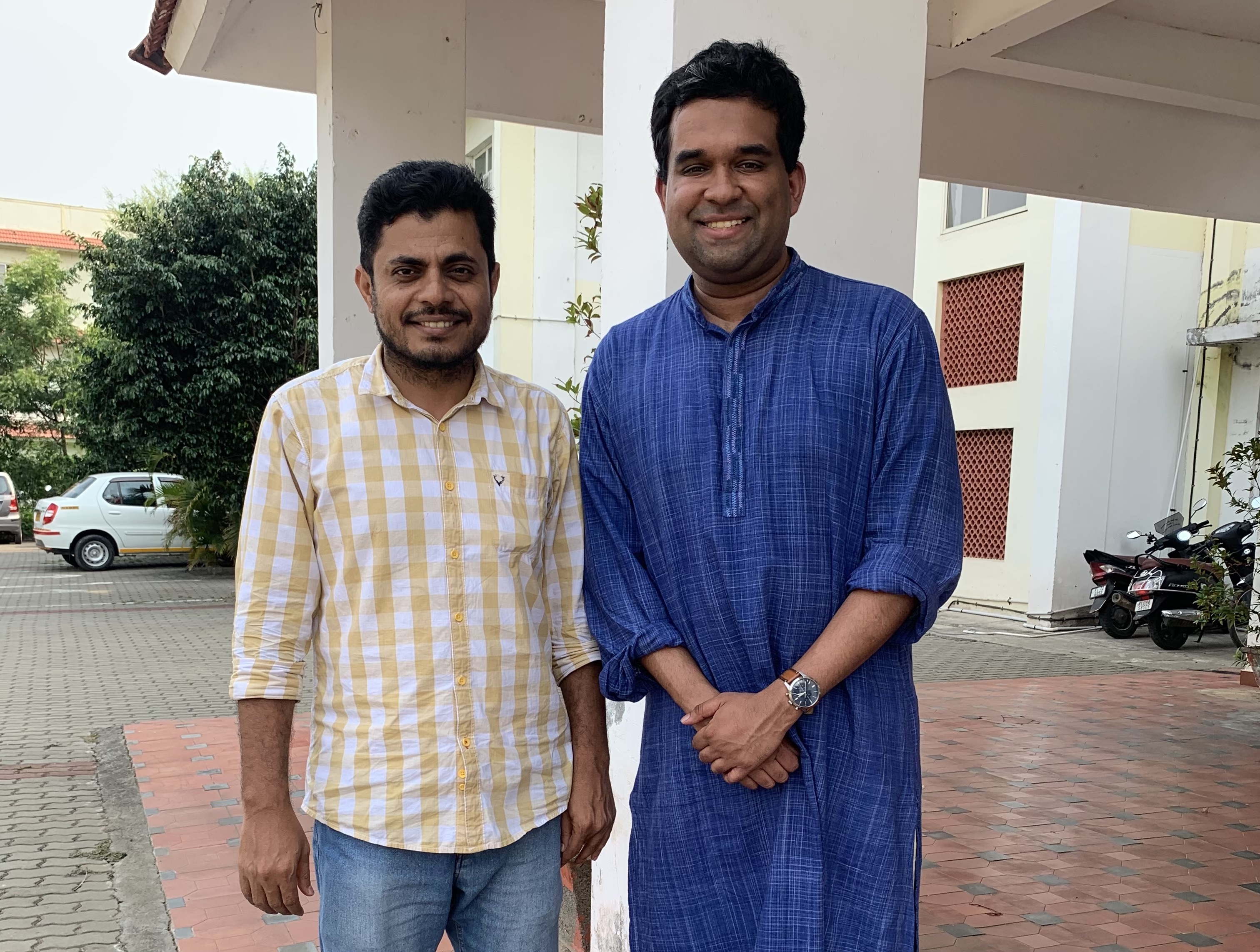 Two men standing together outside a building and smiling for the camera