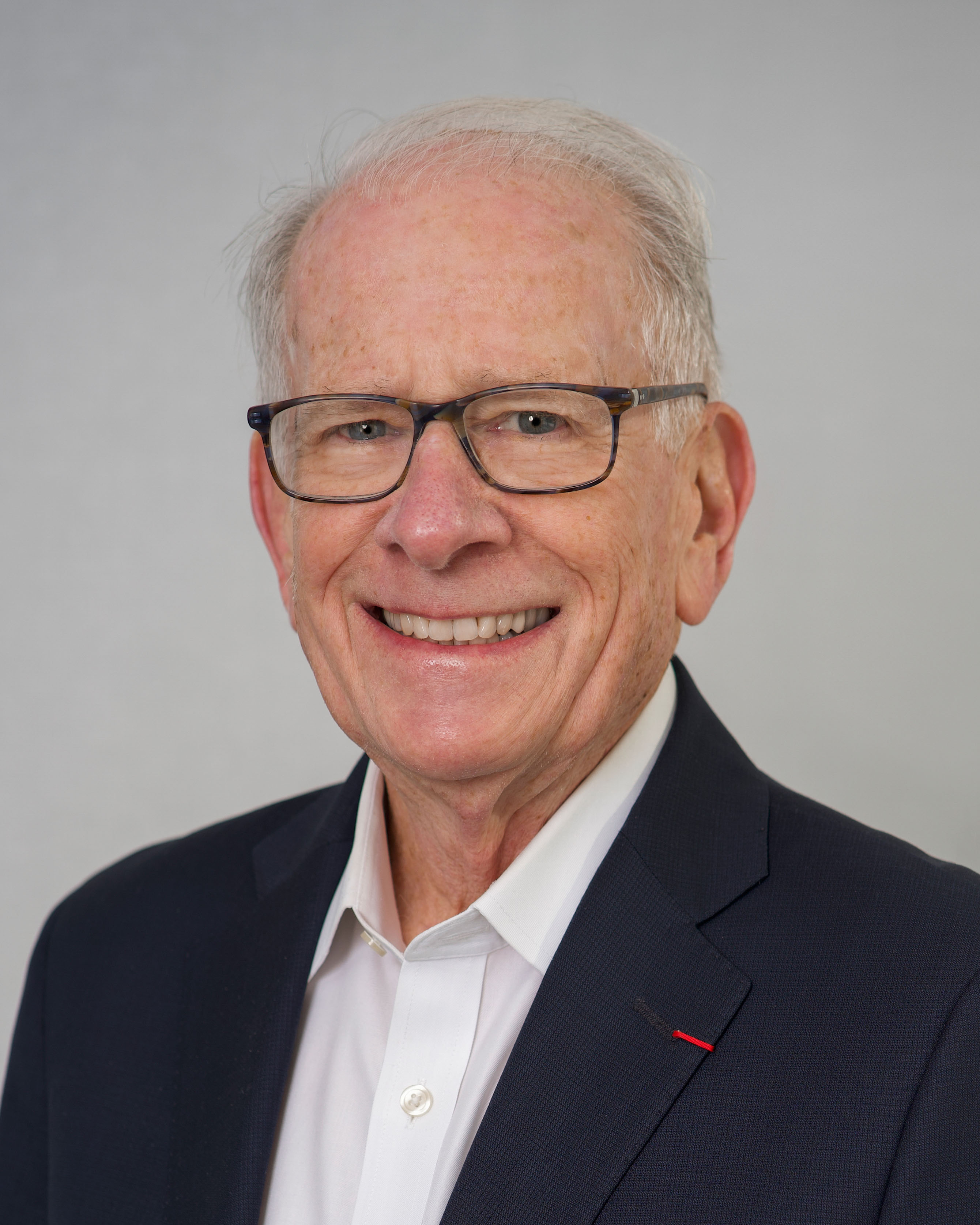 A portrait photo of Allan Goodman, wearing glasses and suit, smiling for the camera