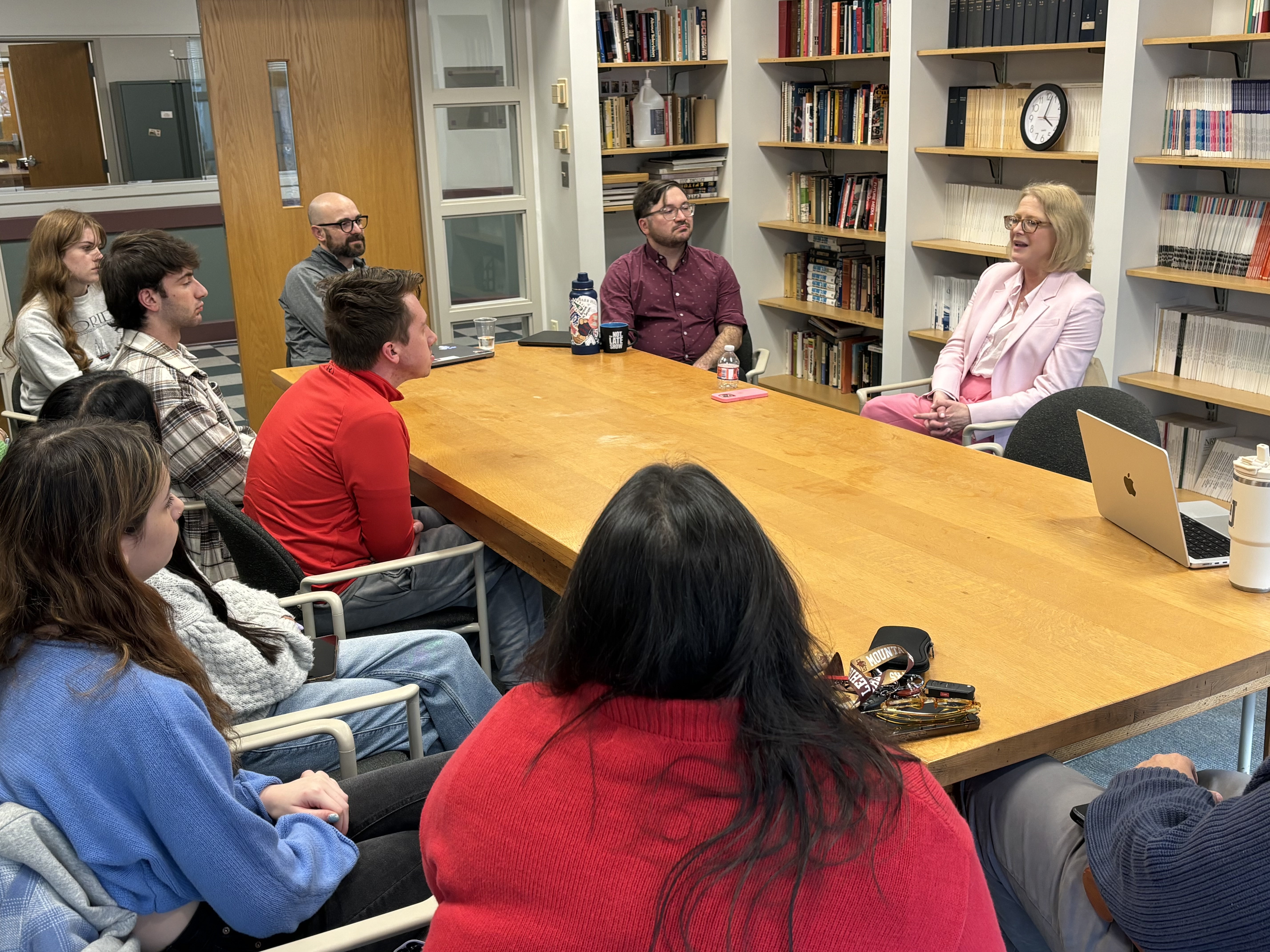 Karin Fischer sitting at a table speaking to several professors and students