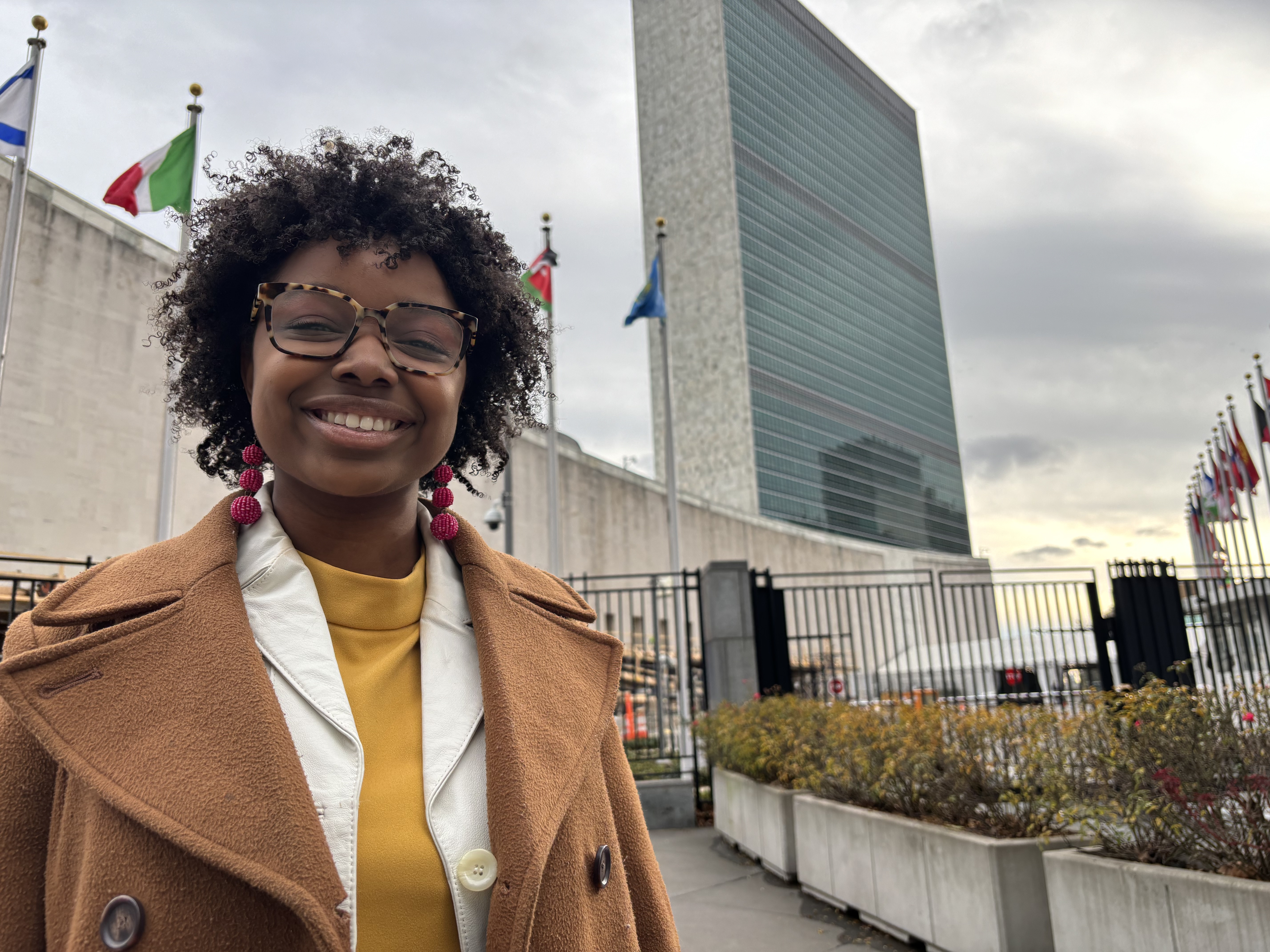 Rhema Hooper standing in front of the United Nations headquarters, smiling for the camera