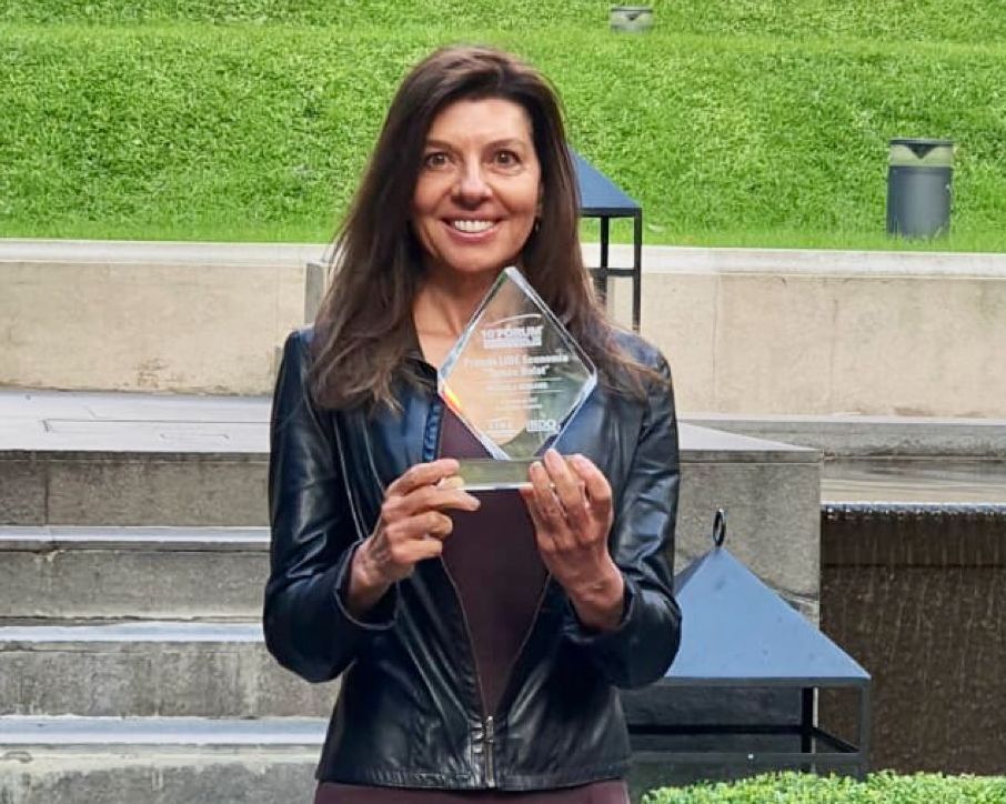 A woman holding an award while standing in front of a building