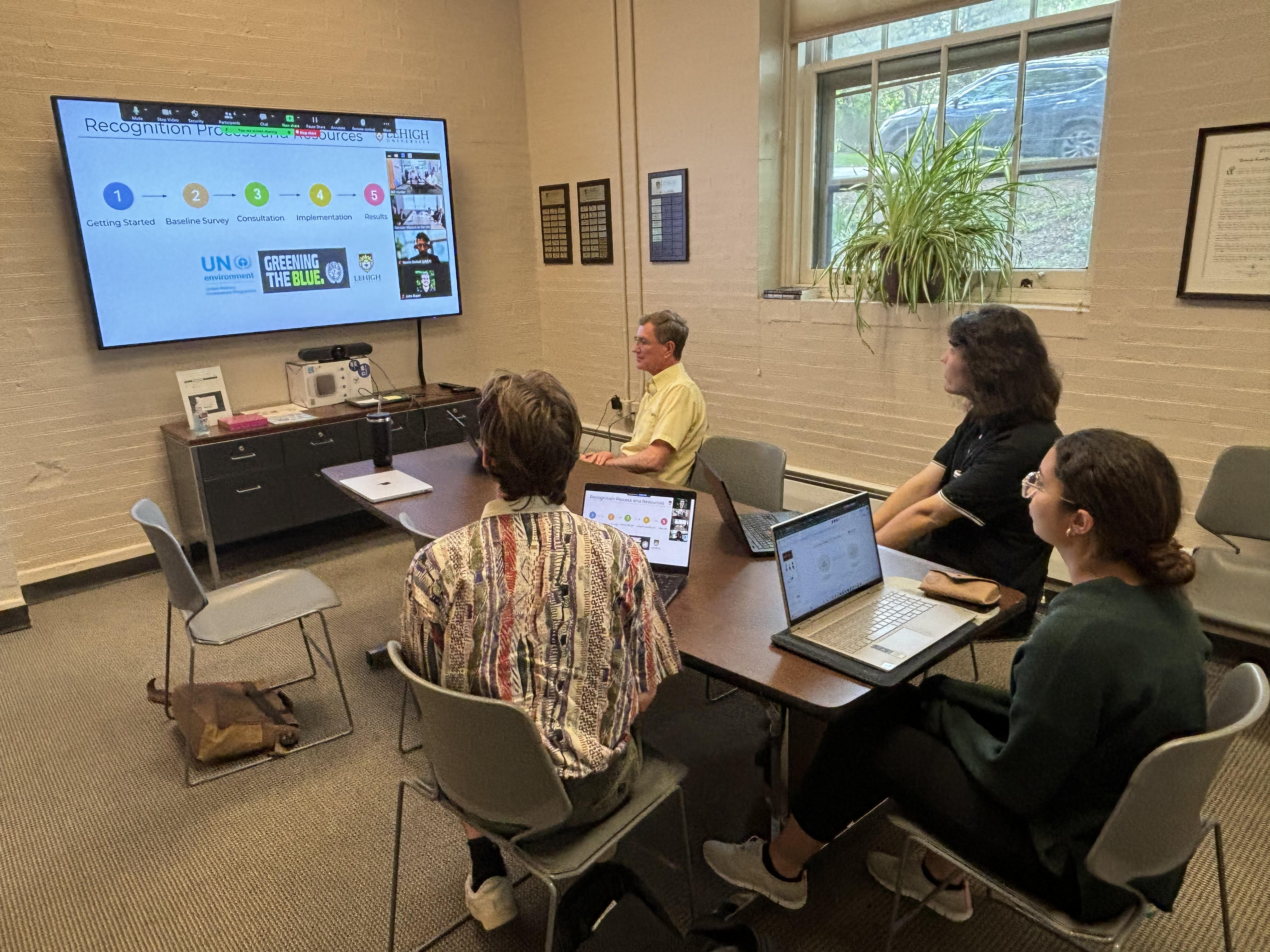 Four people giving a Powerpoint presentation in a conference room