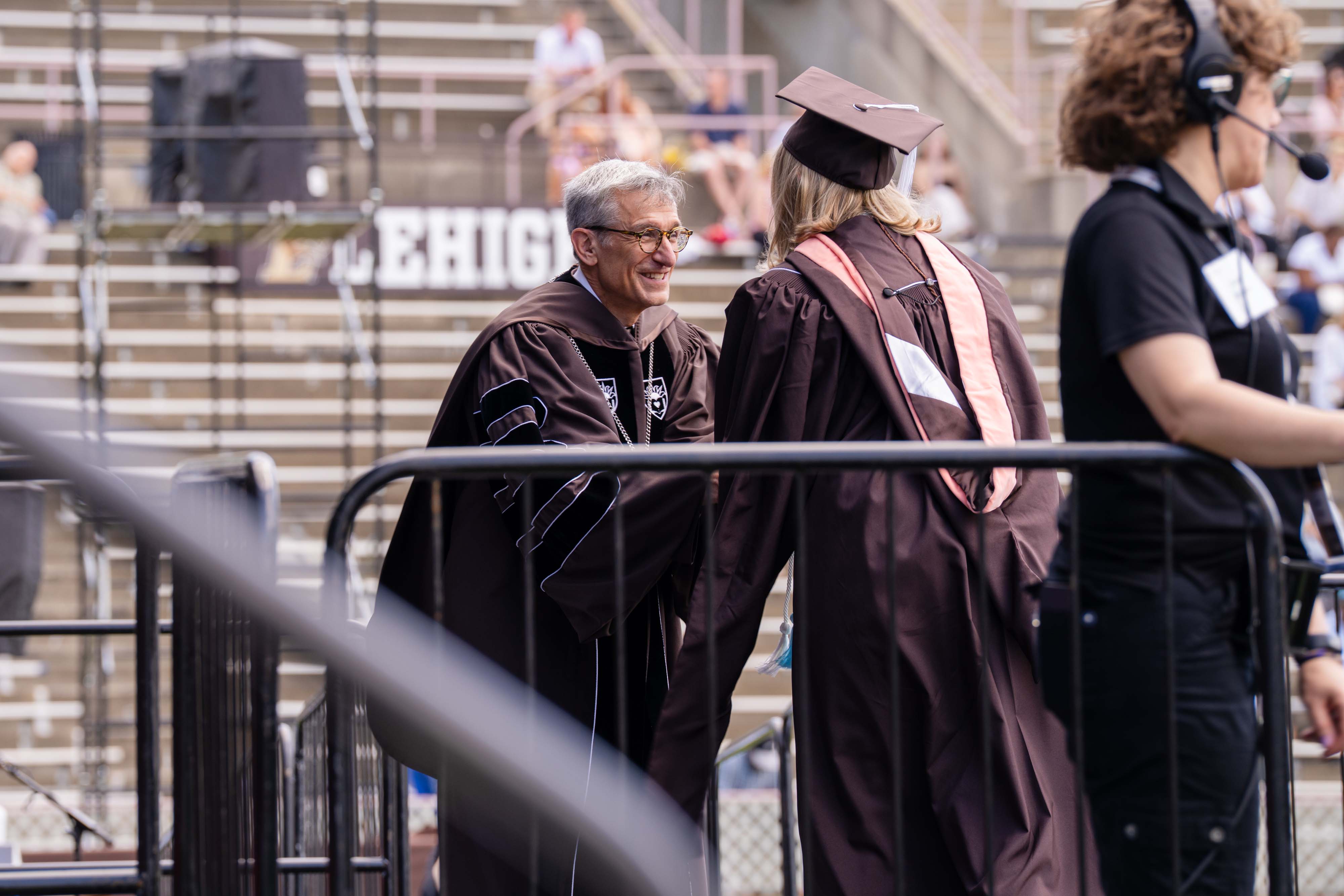 A man in brown robes shaking a young woman's hands at a graduation commencement