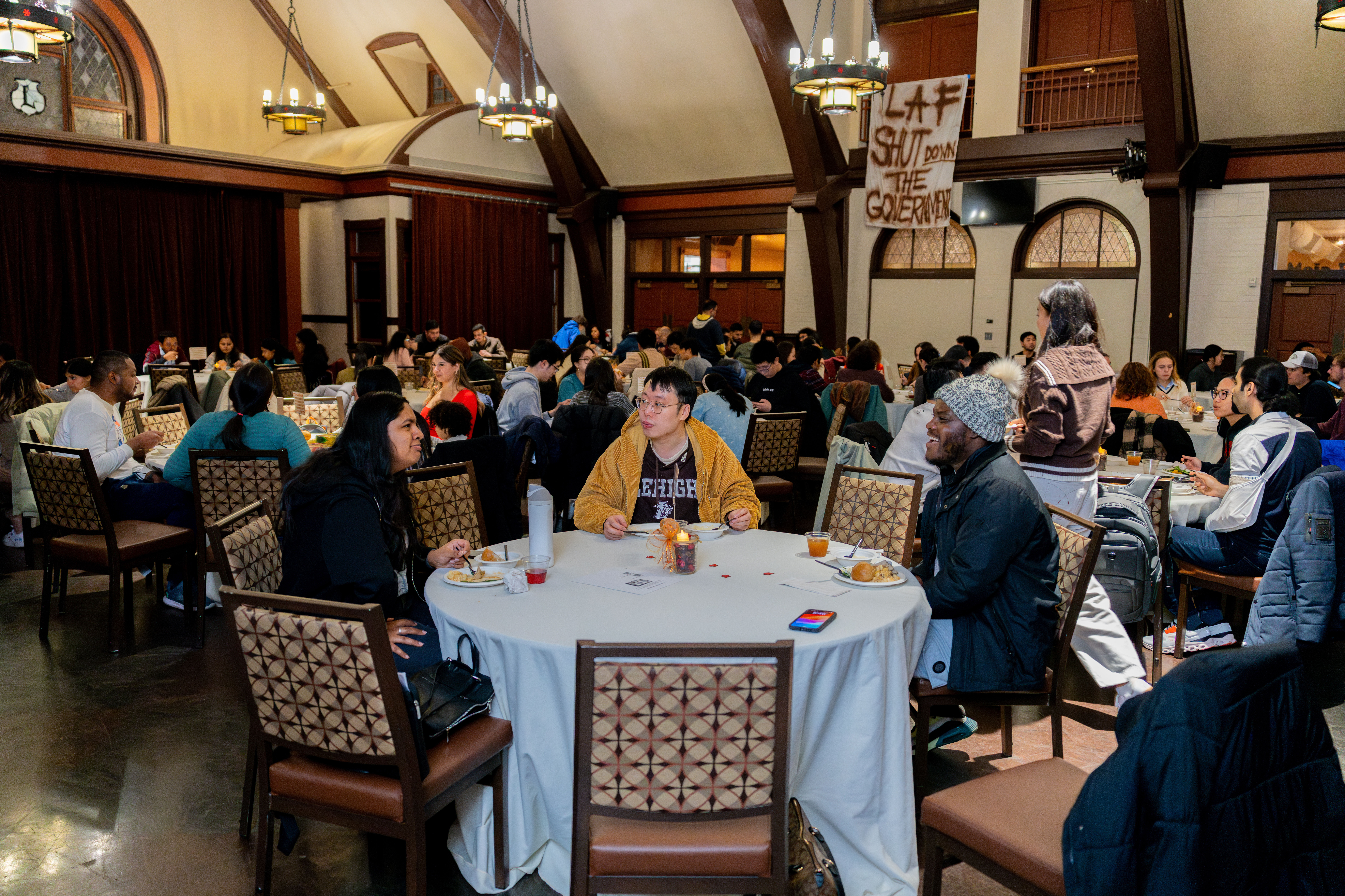 A large group of students at tables, eating dinner in a large hall