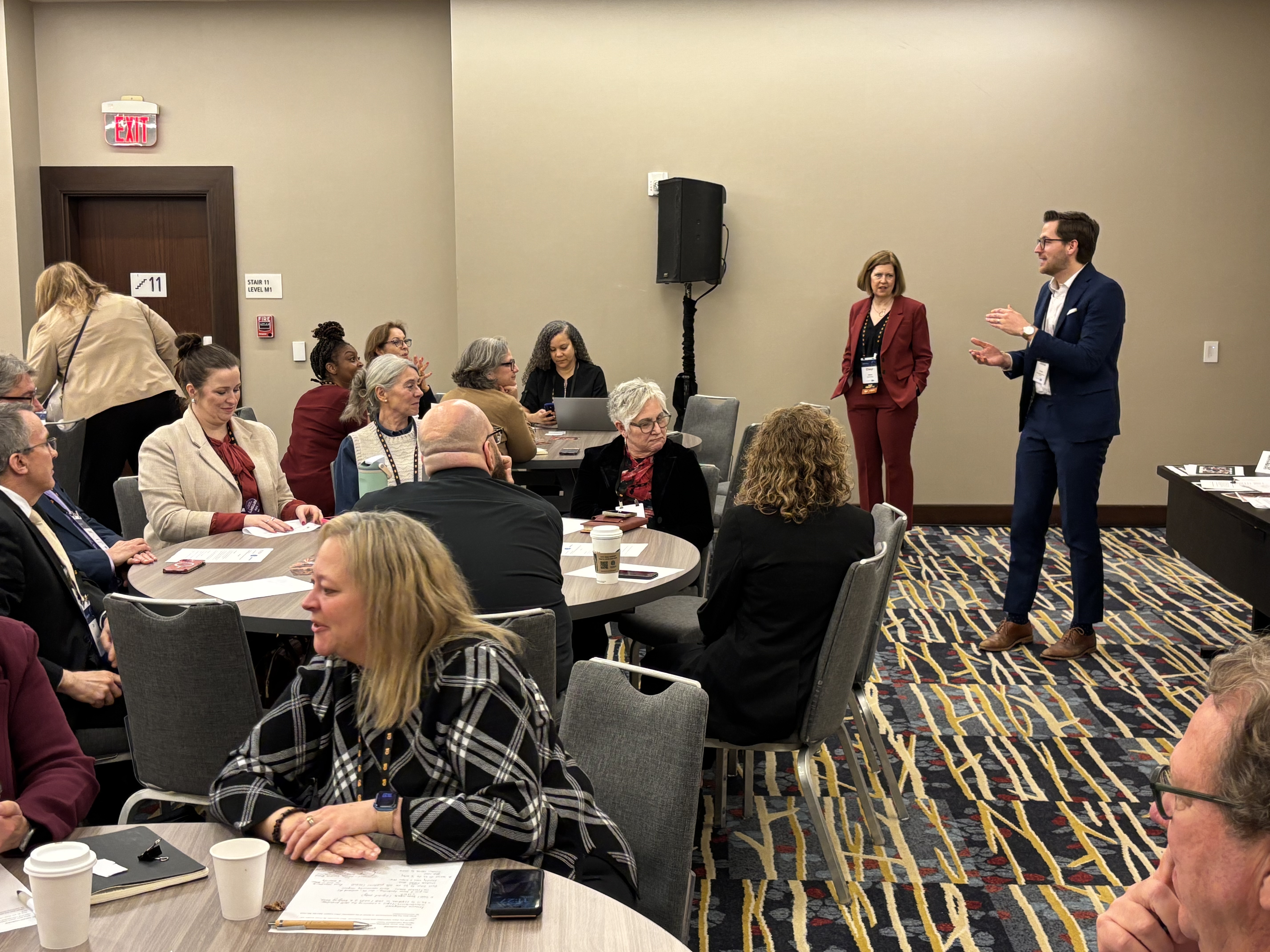 A man and woman speaking to a group in a conference room