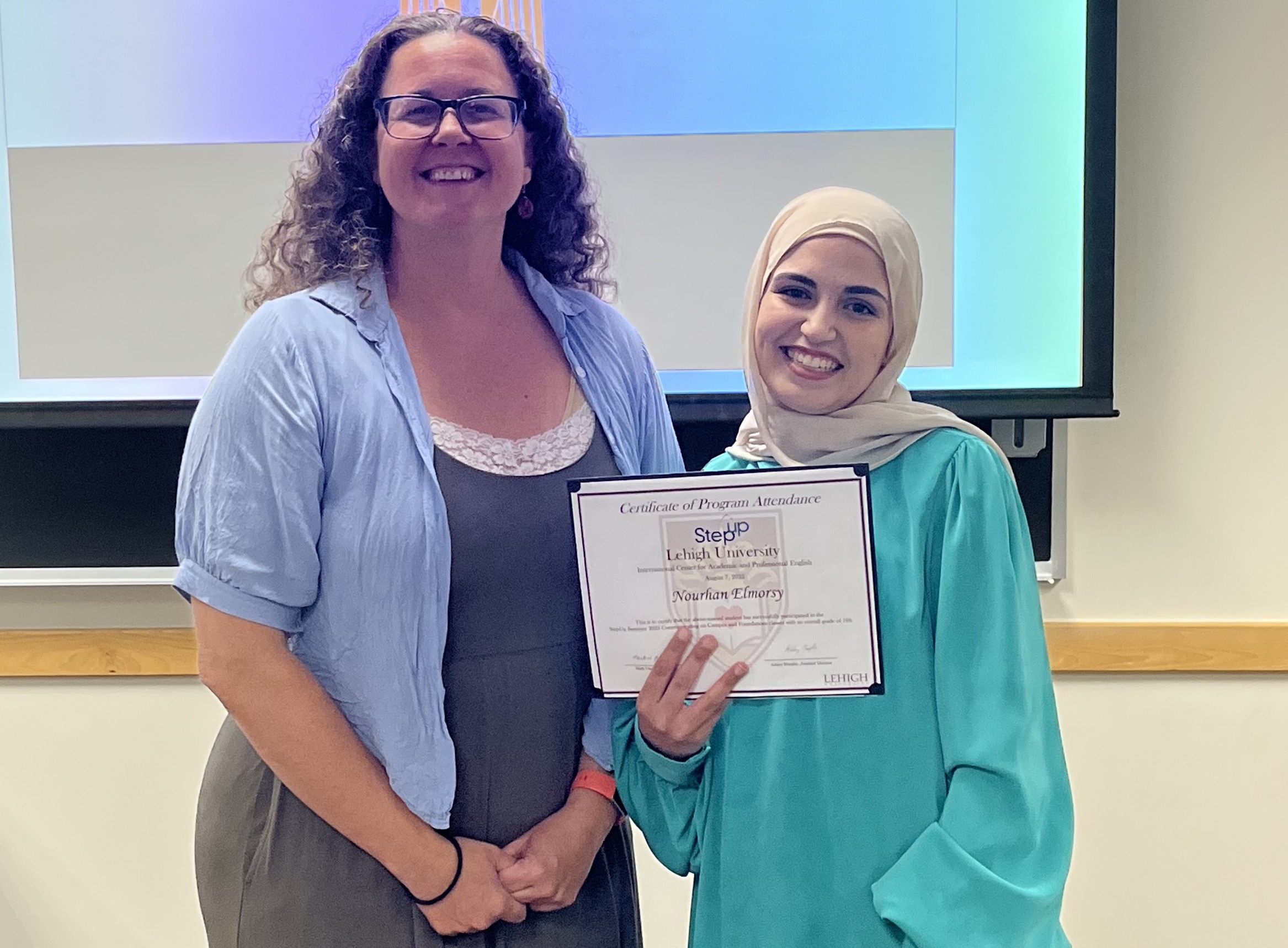 Two women standing together and smiling for the camera, with one holding a certificate