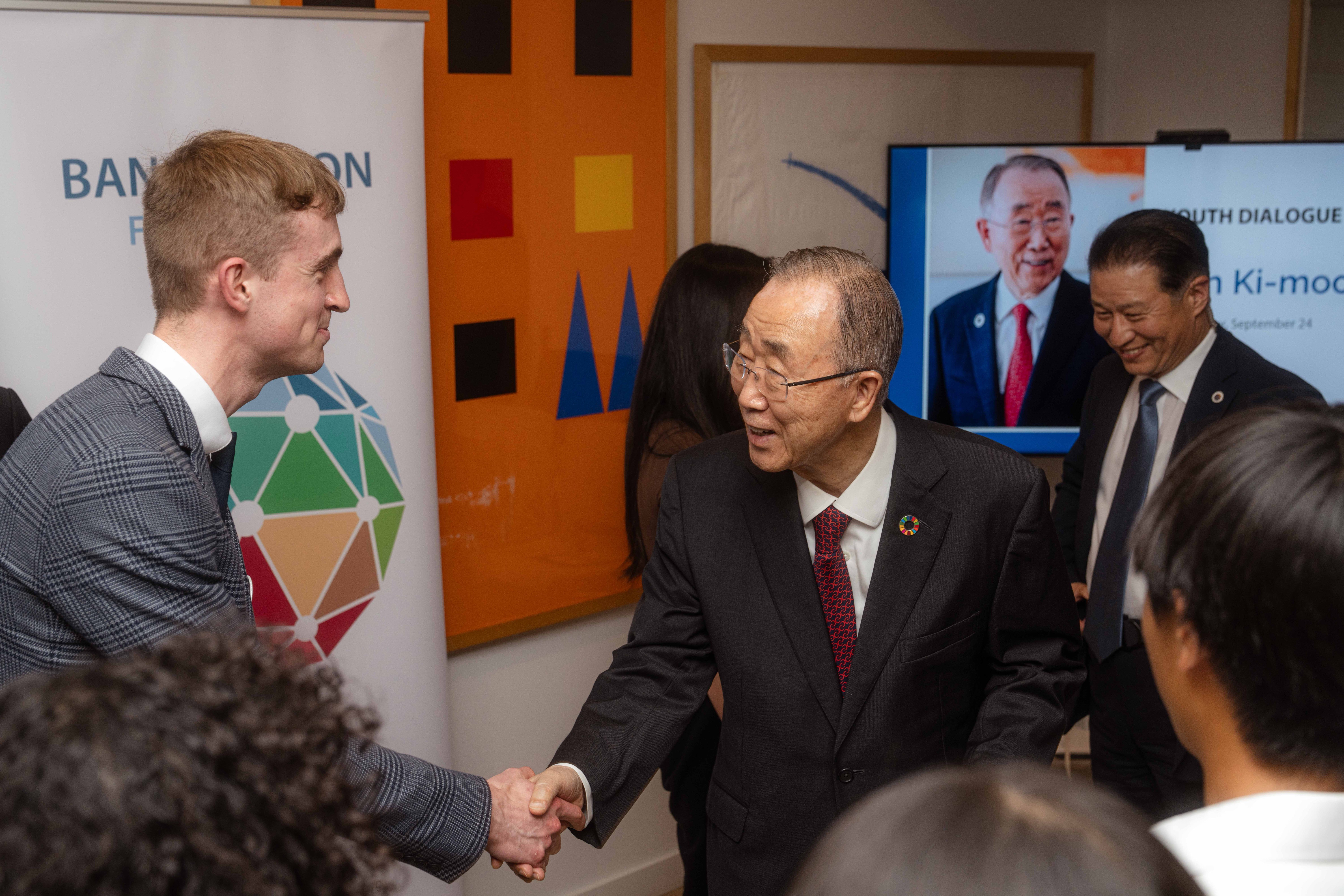 Ban Ki-moon shakes hands with a young man in a suit at the United Nations headquarters