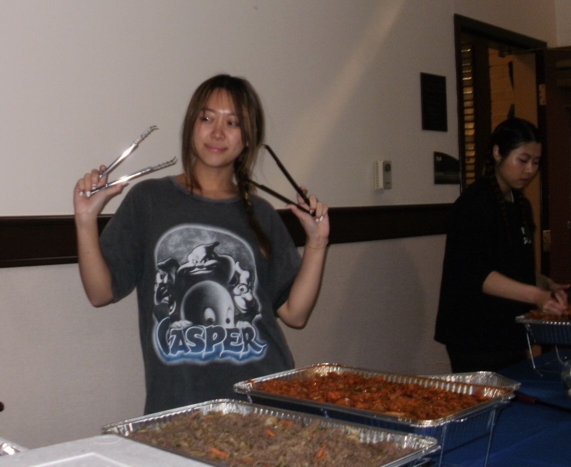 A young woman holding a pair of tongs while standing in front of a buffet