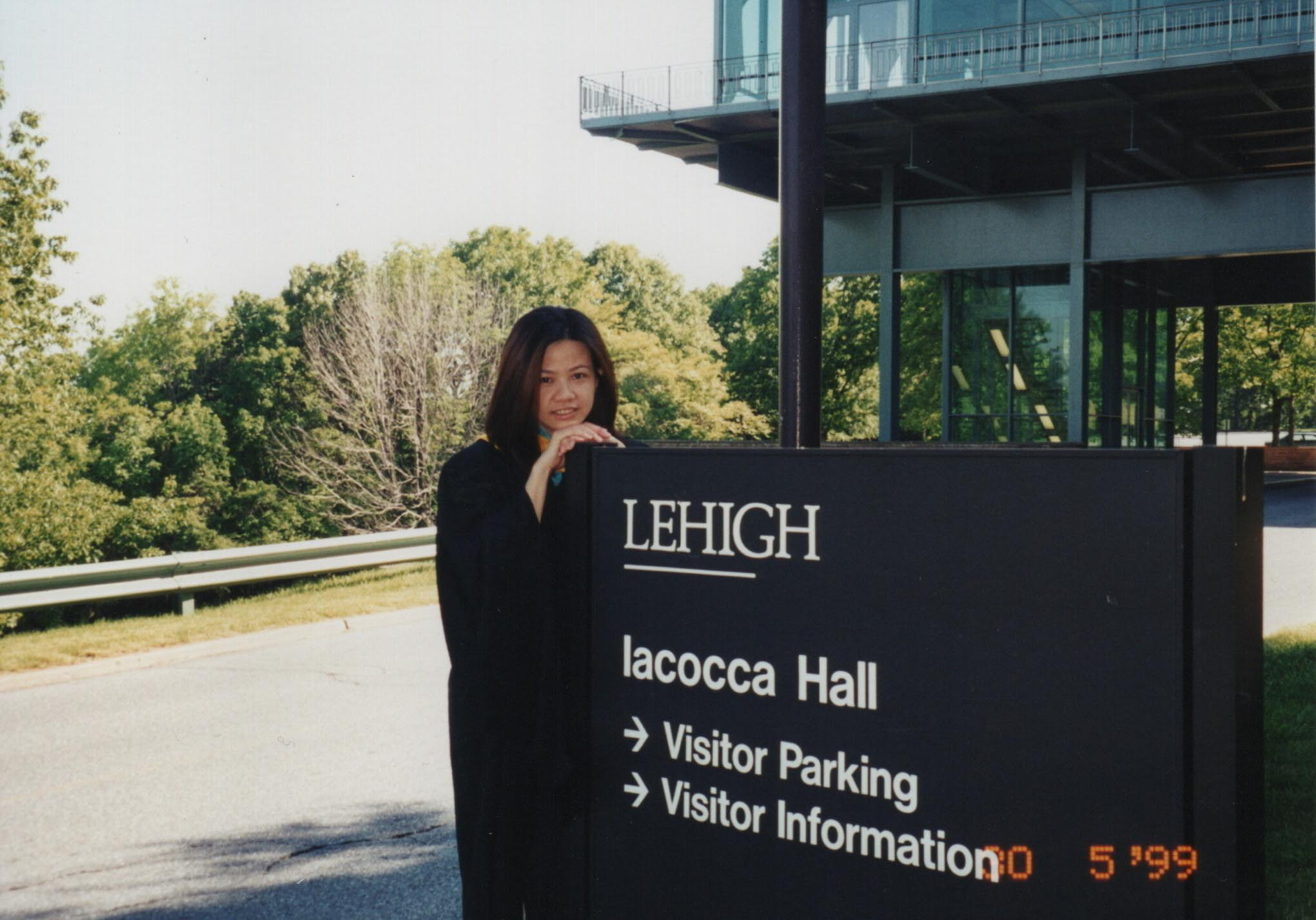 A woman leaning against a Lehigh University sign while wearing a graduation robe