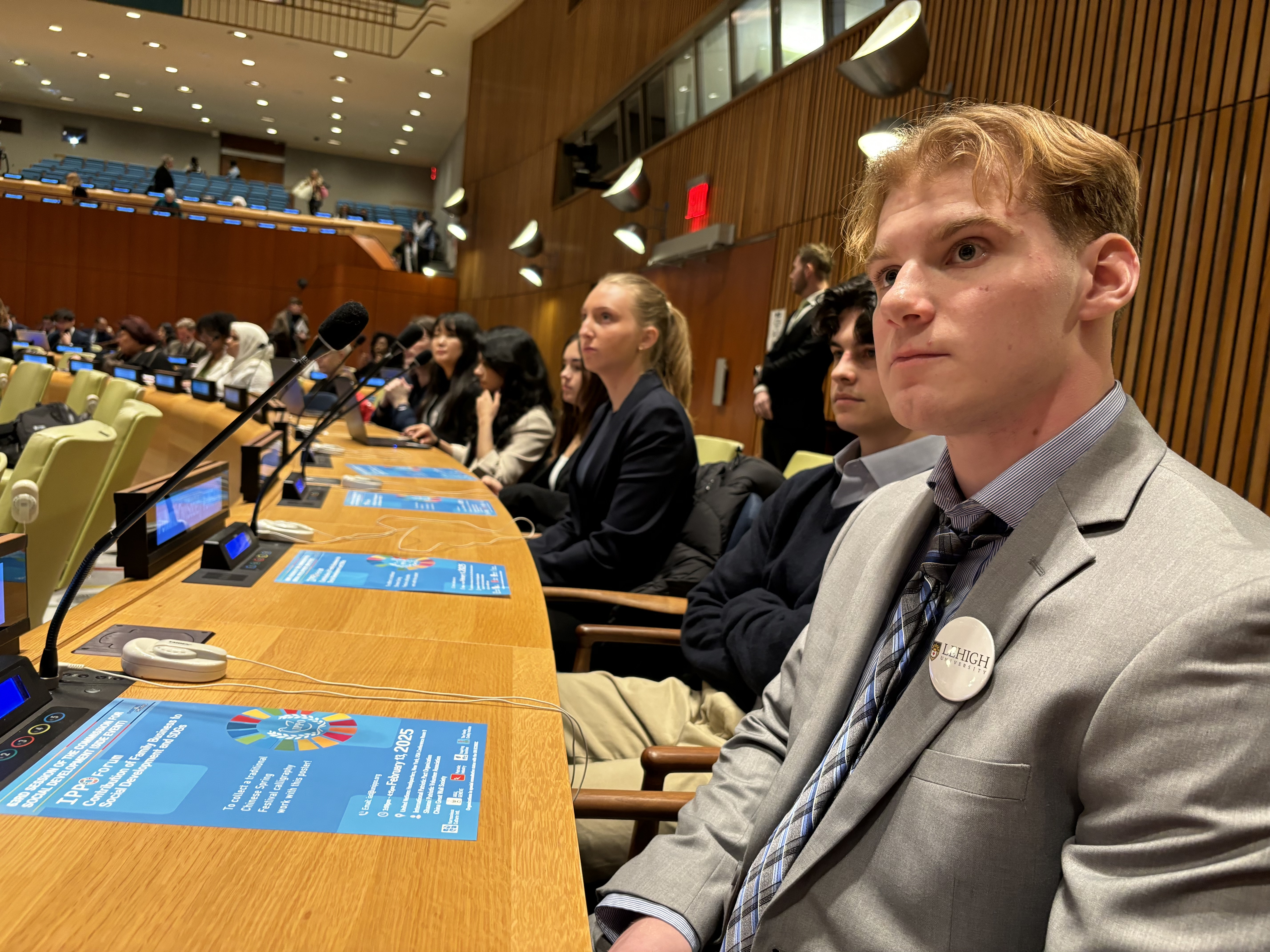 A young man in the foreground looking off-camera in a United Nations chamber