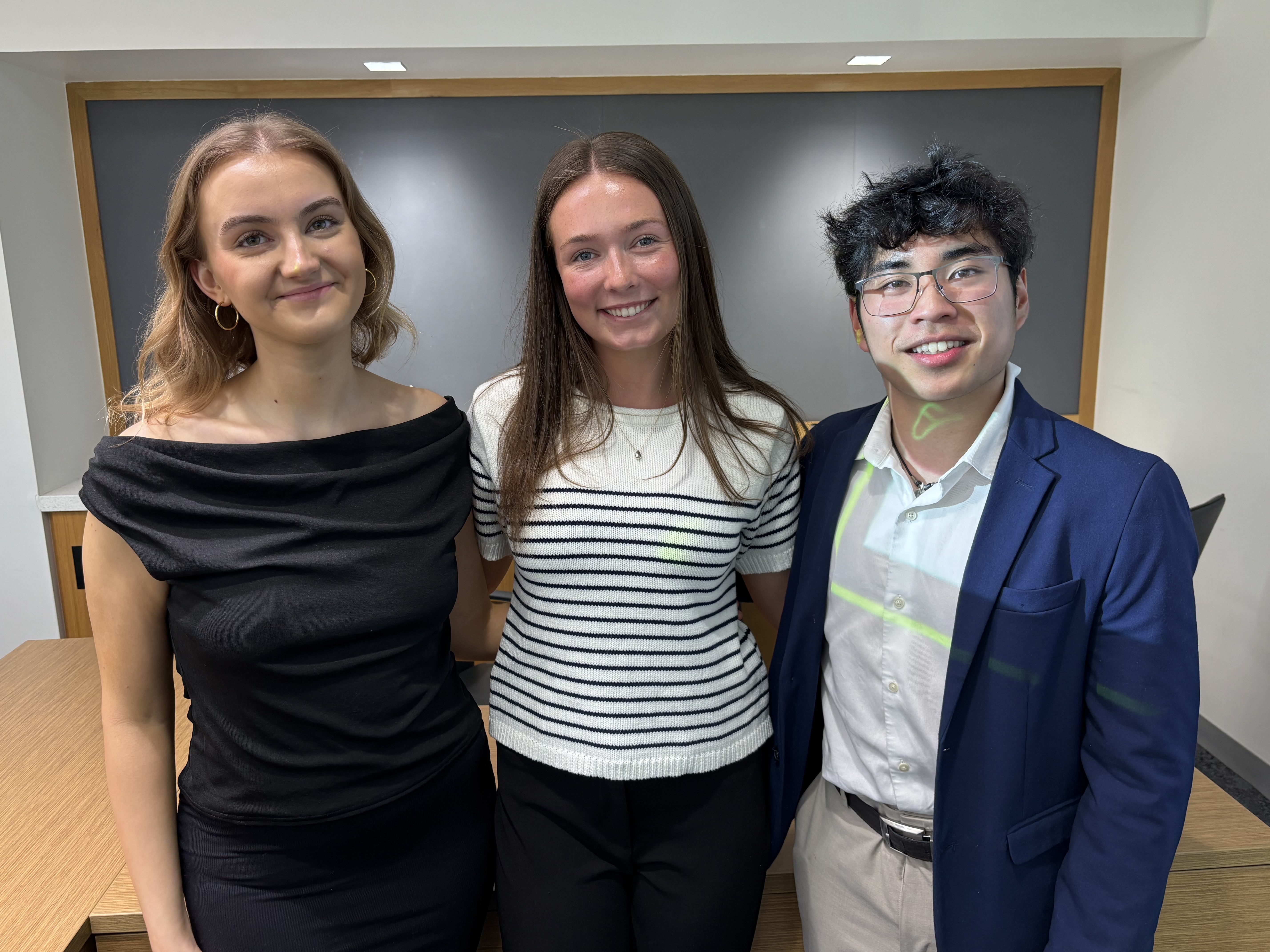 A group of three college students standing together and posing for the camera