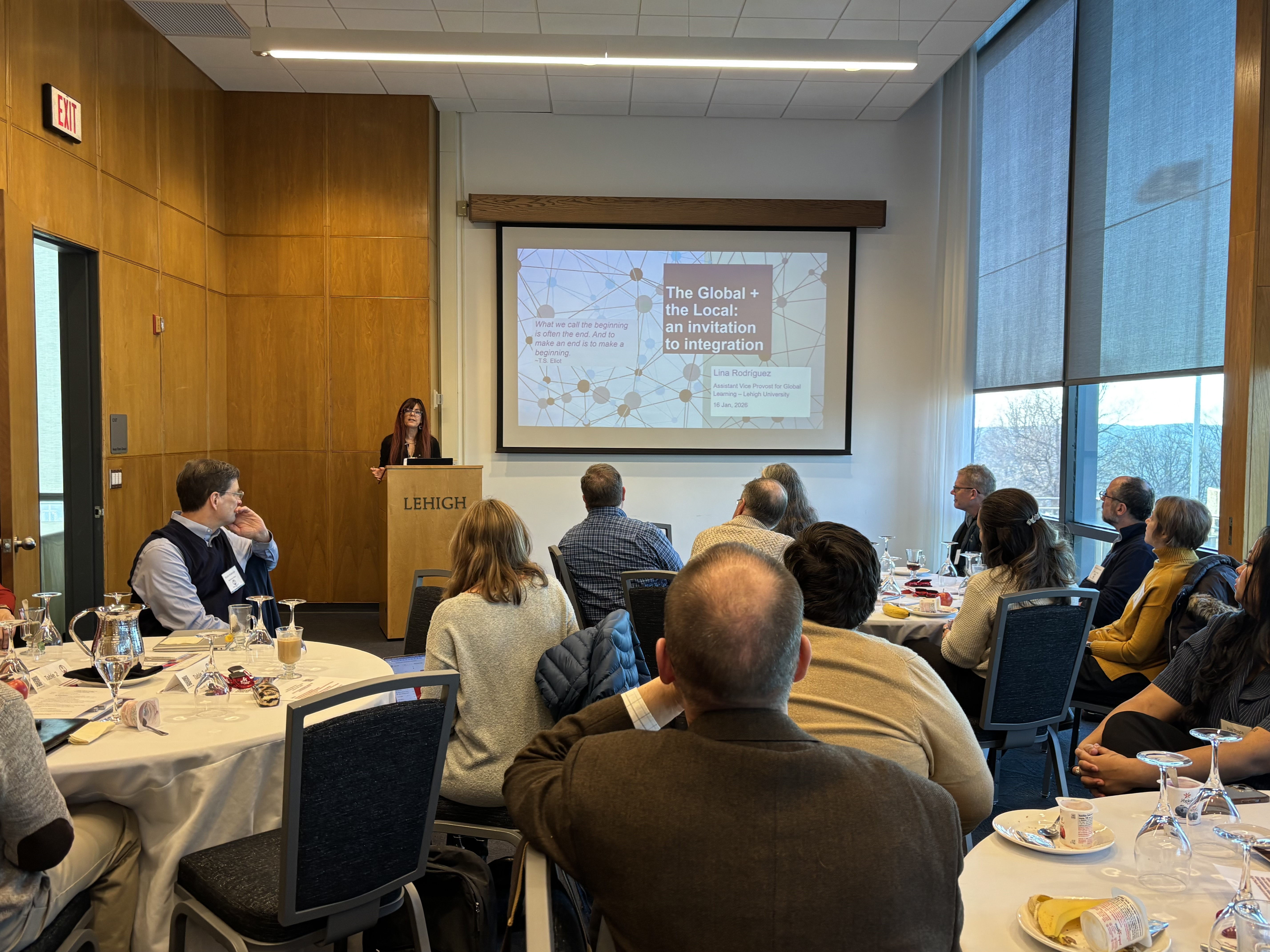 A woman speaking at a podium to several people sitting at tables