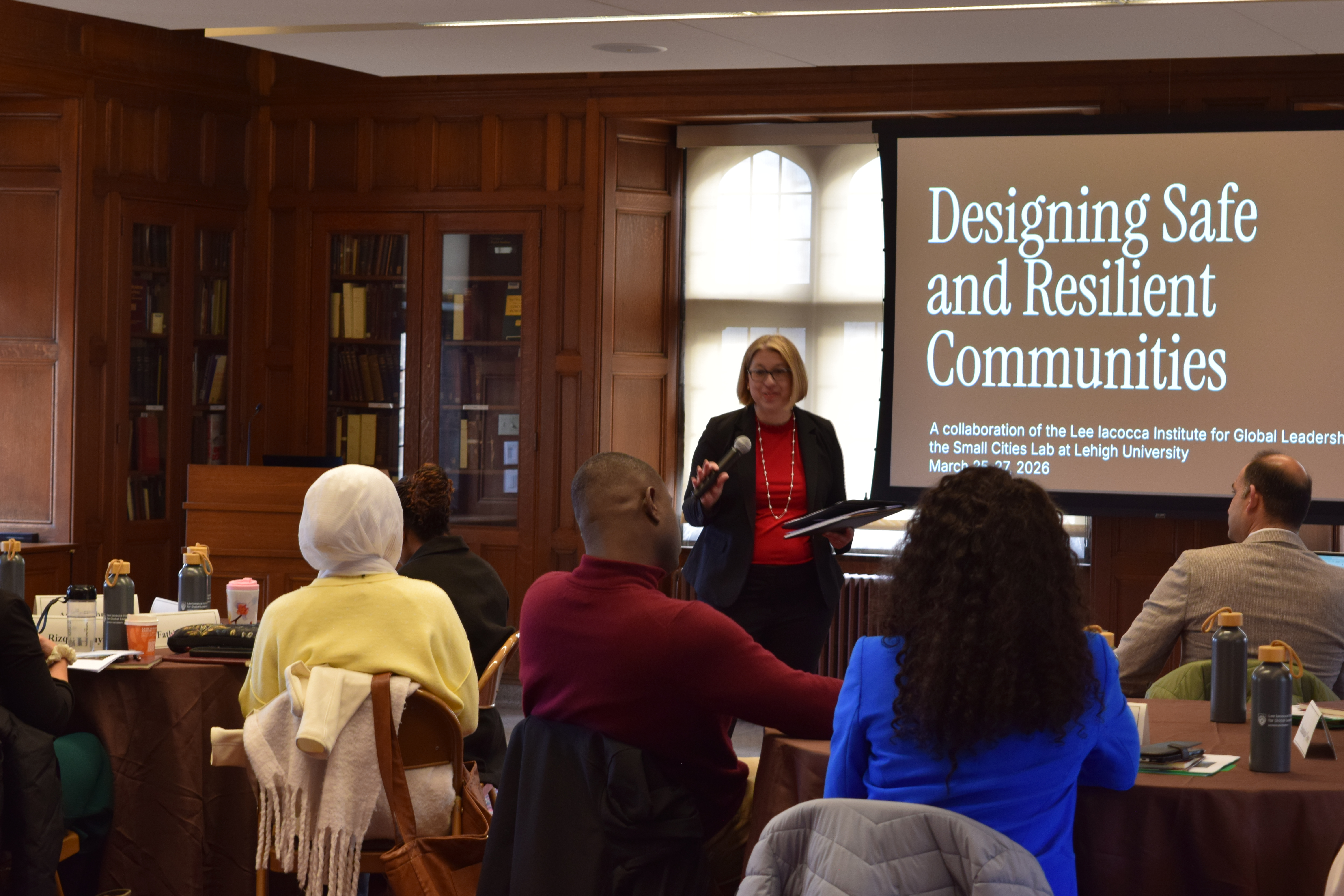 A woman with a microphone speaking in front of a screen that says Designing Safe and Resilient Communities