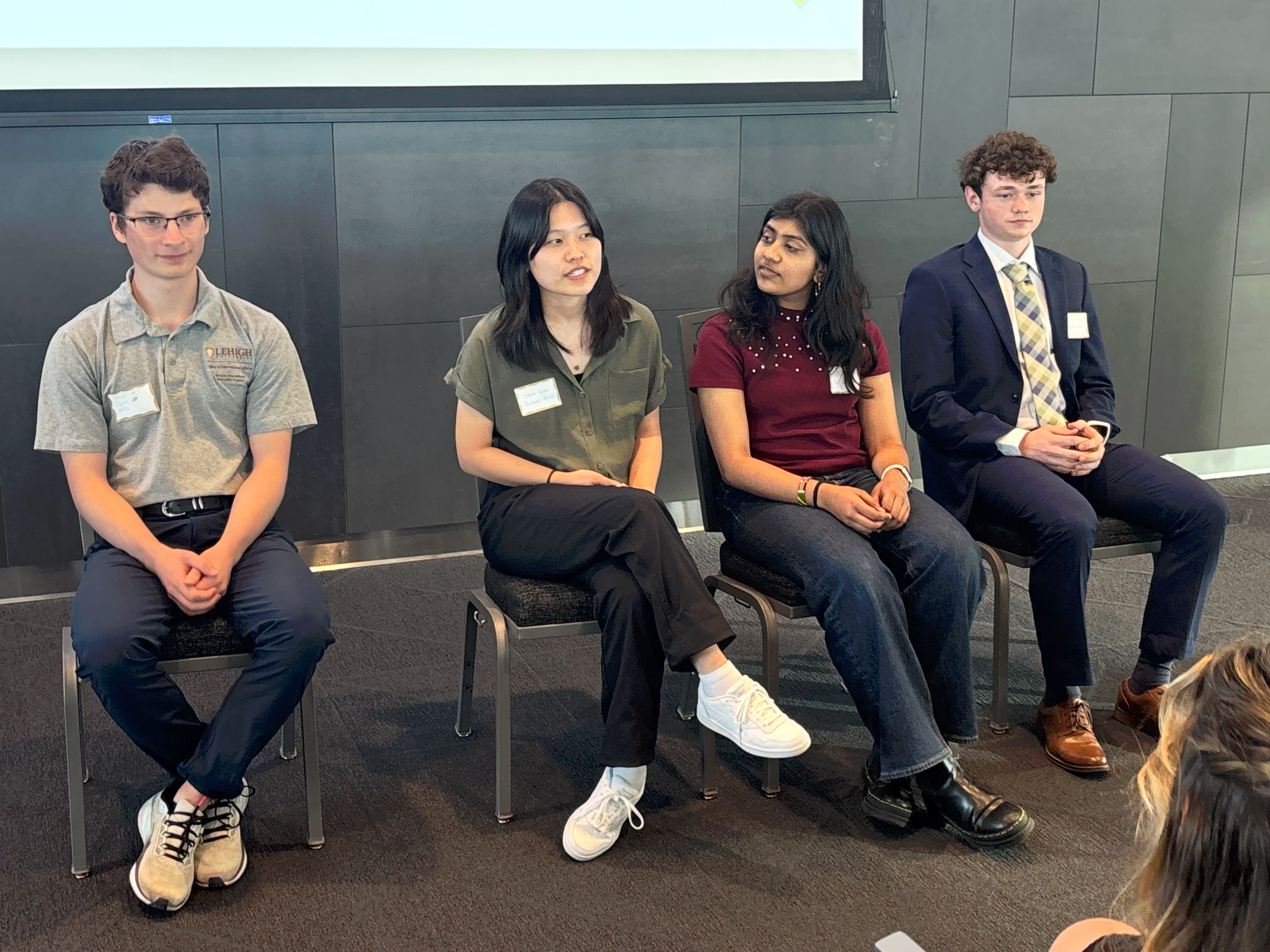 Four college students sitting in chairs, talking to a crowd