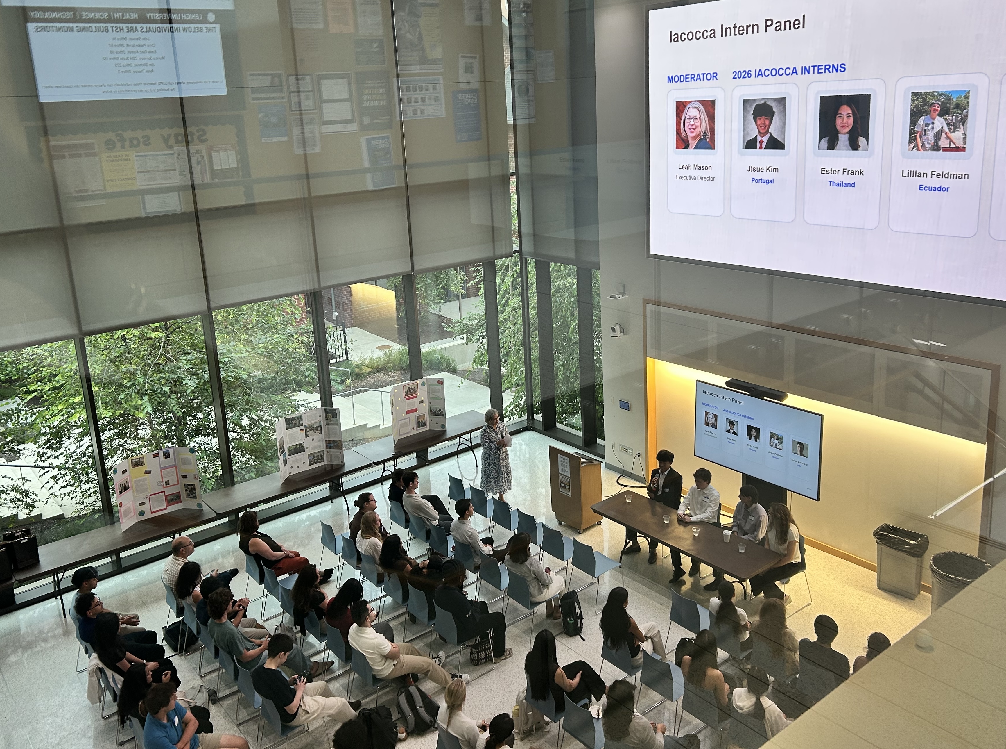 A group of people sitting in a high-ceiling room watching a Powerpoint presentation