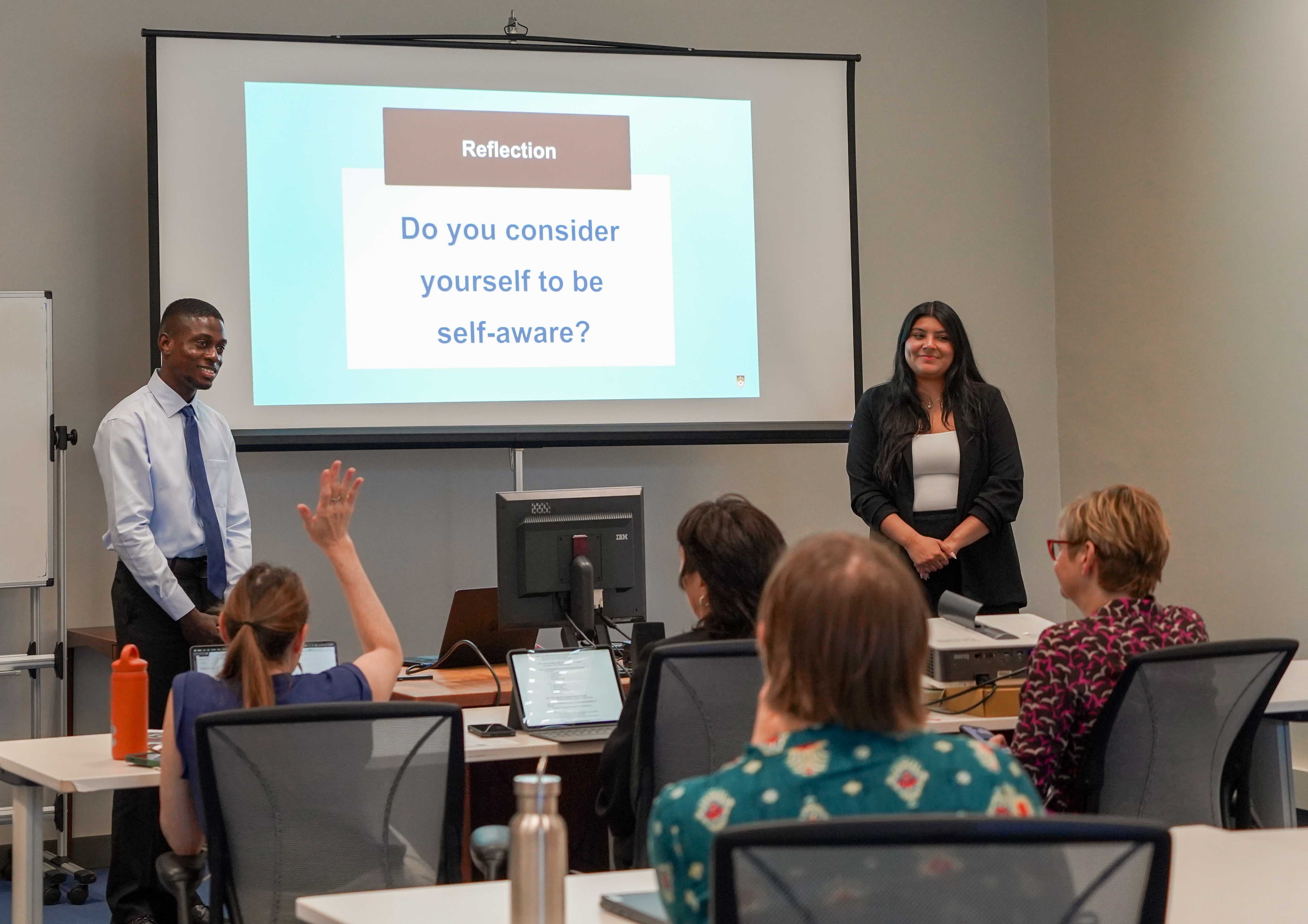 Two young people presenting before an audience in front of an overhead projector