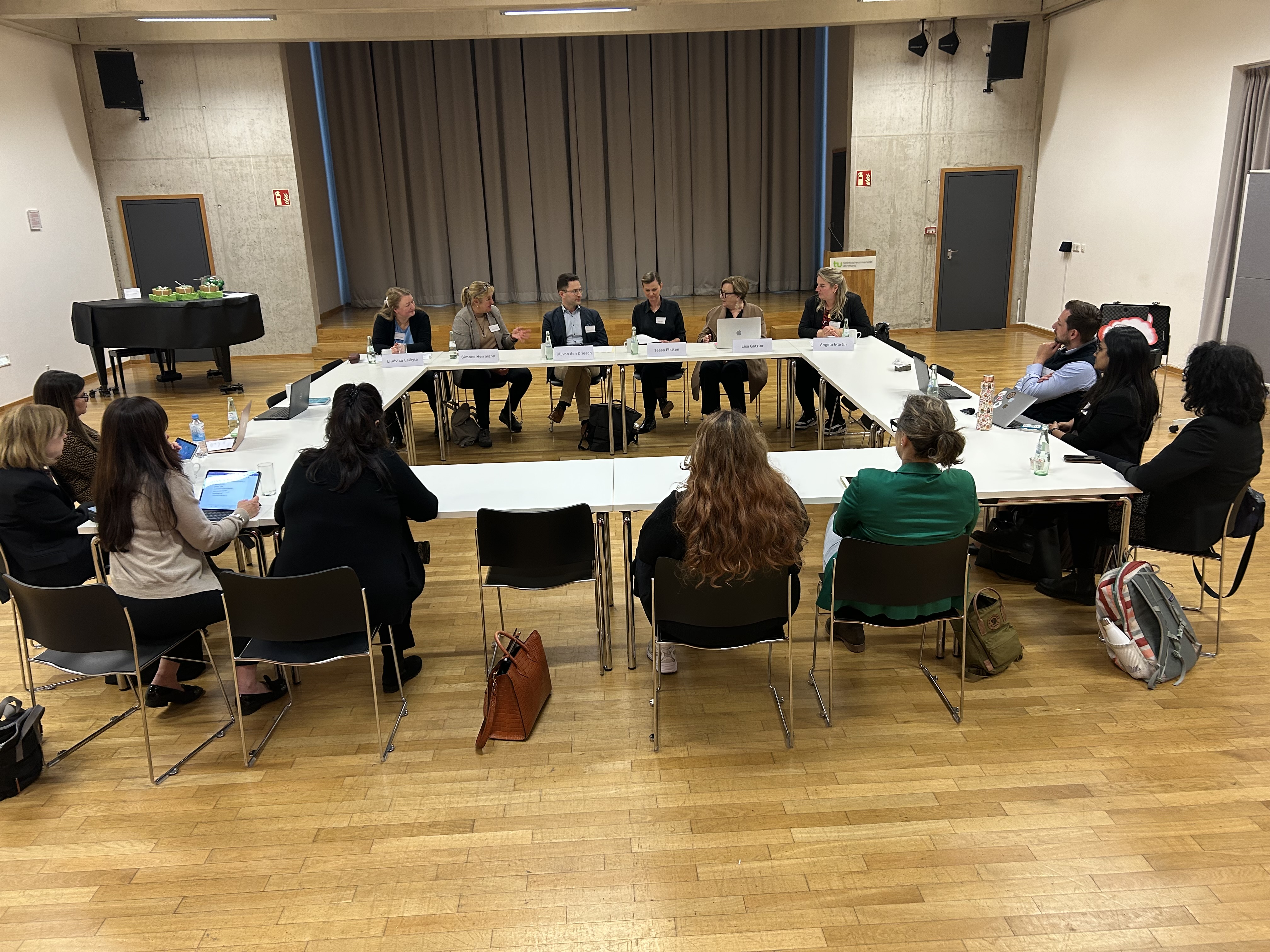 Several people gathered around a set of tables set up in a square formation