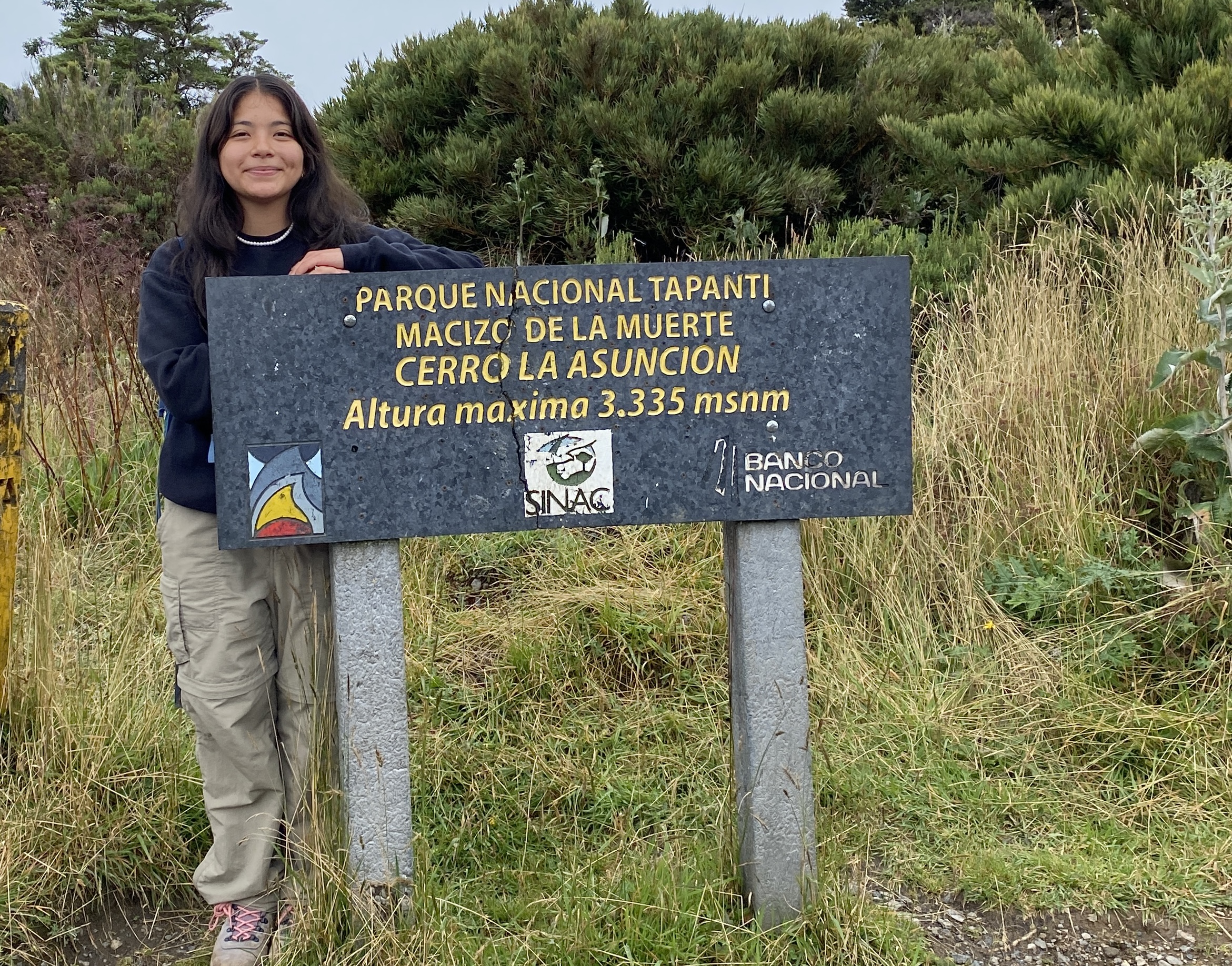 A young woman standing next to a sign at Cerro La Asunción in Parque Nacional Tapantí–Macizo de la Muerte in Costa Rica