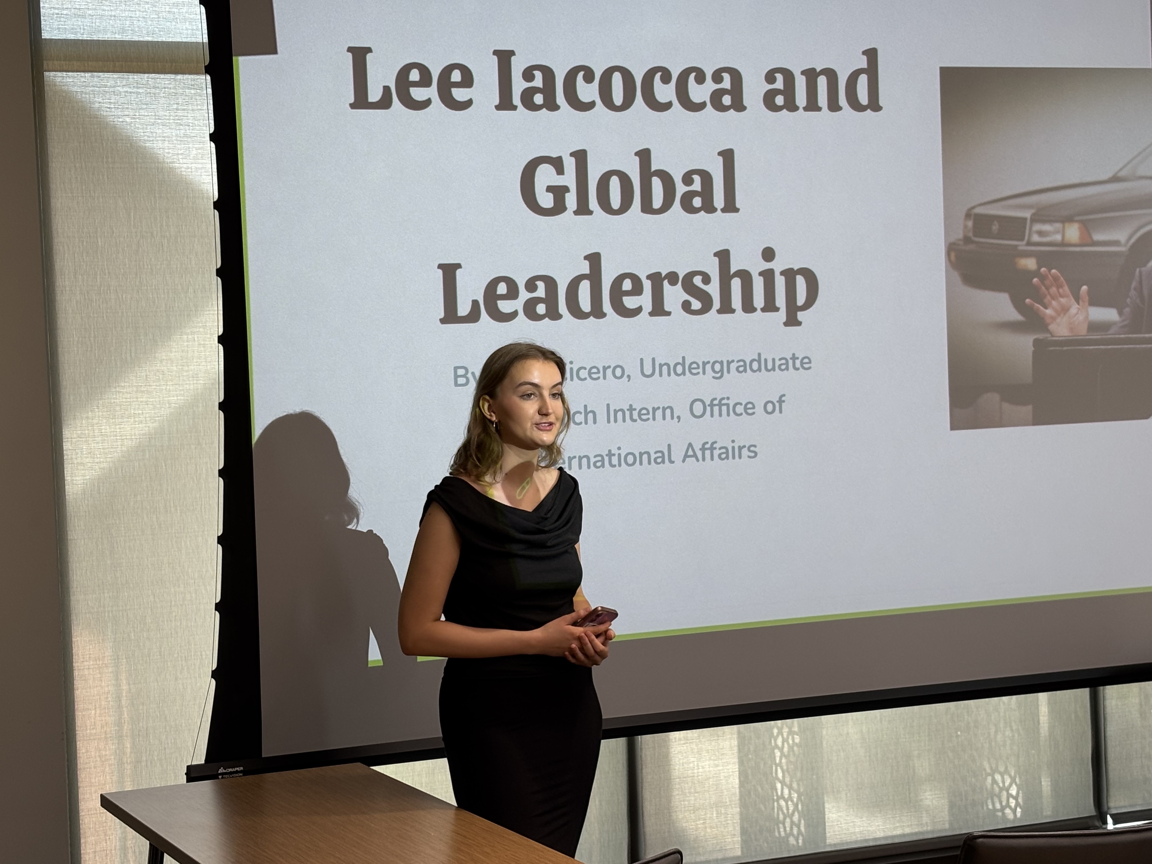 A young woman speaking in front of a Powerpoint screen