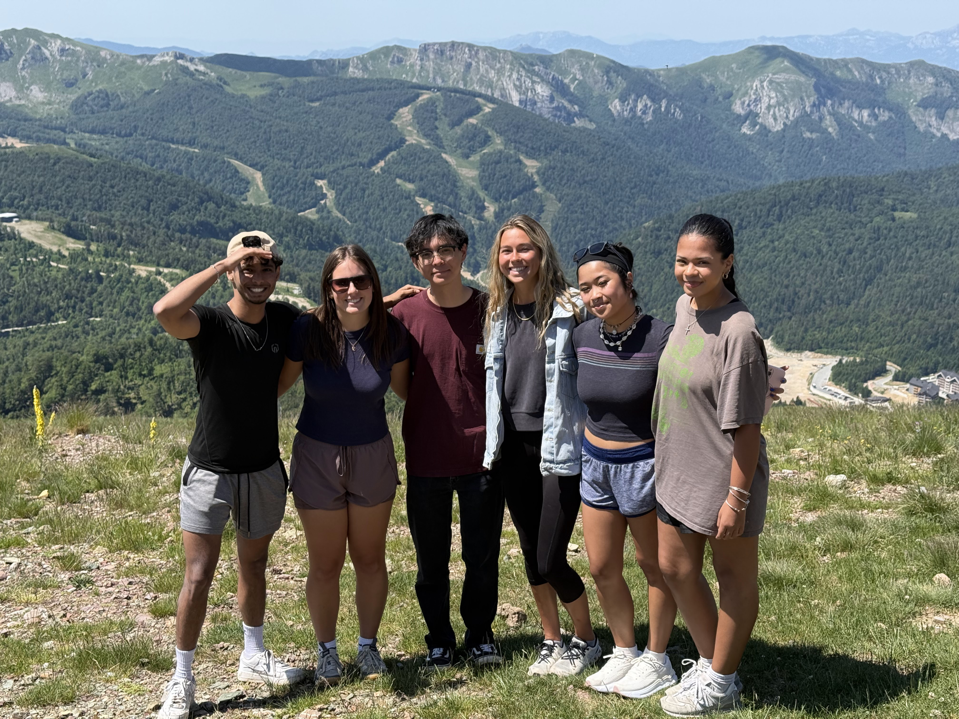 Six students posing for a photo outside on a grassy hill