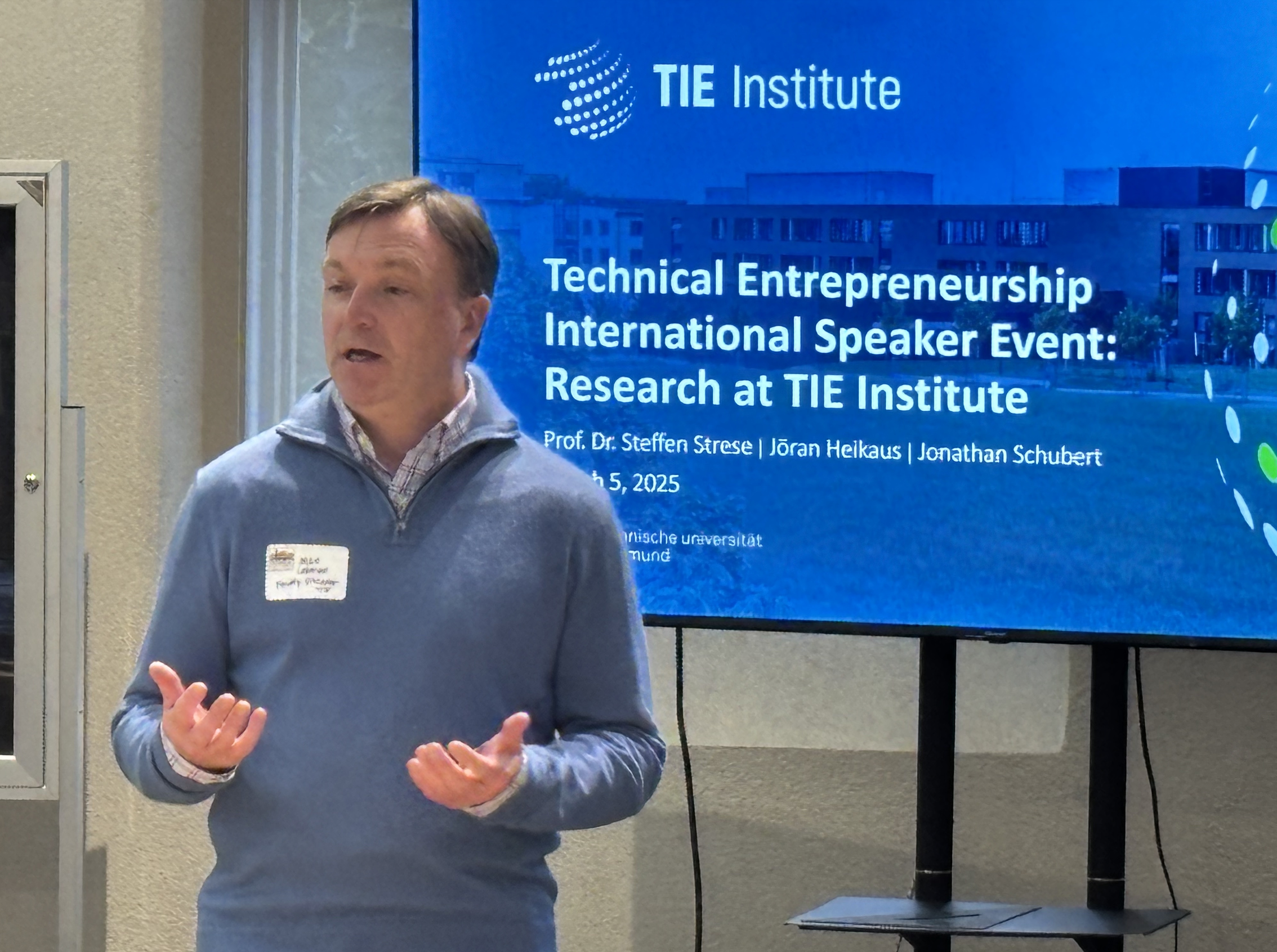 A man in a blue shirt talks in front of a projector screen