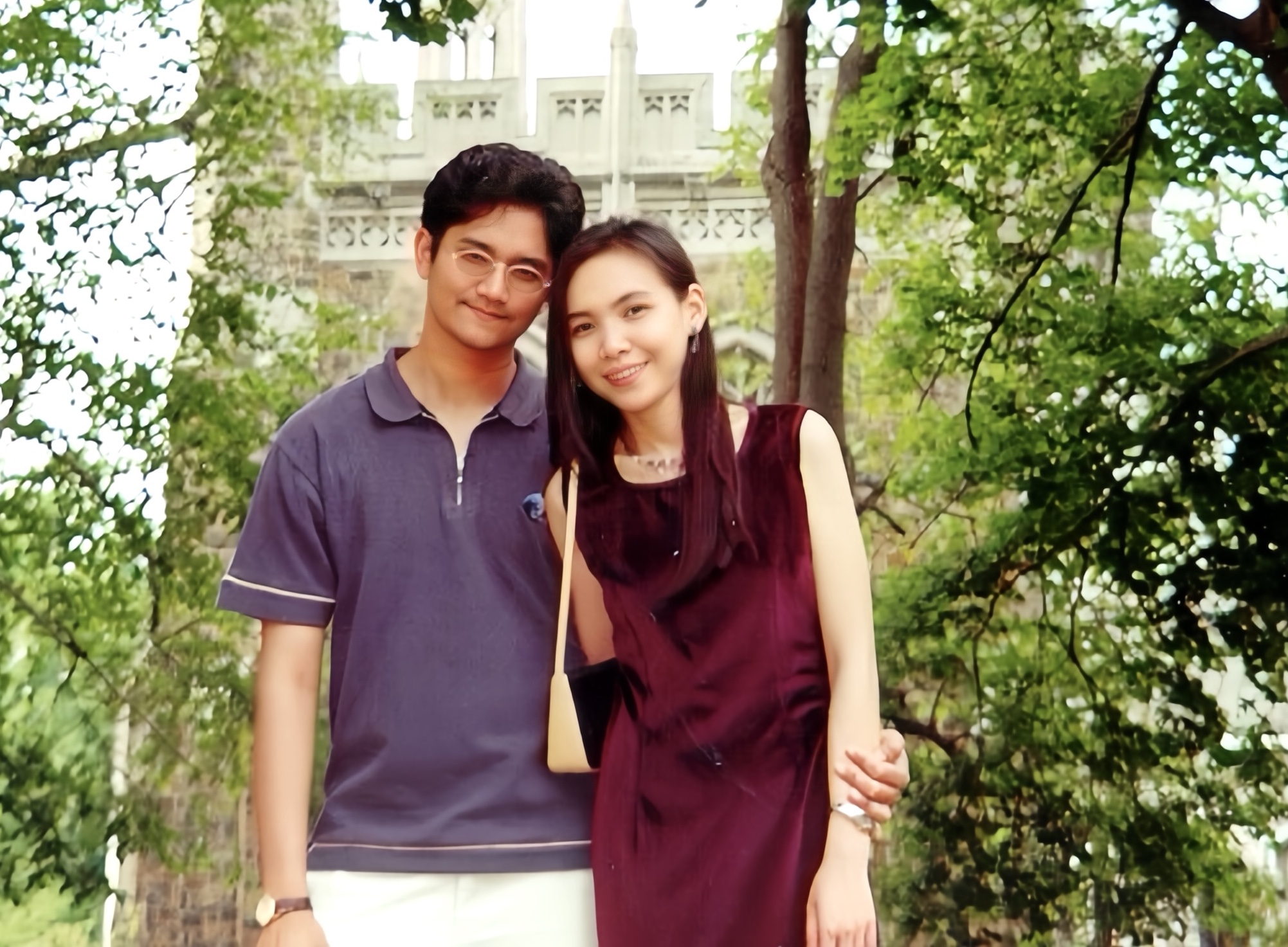 Two people standing in front of a building and some trees, smiling for the camera