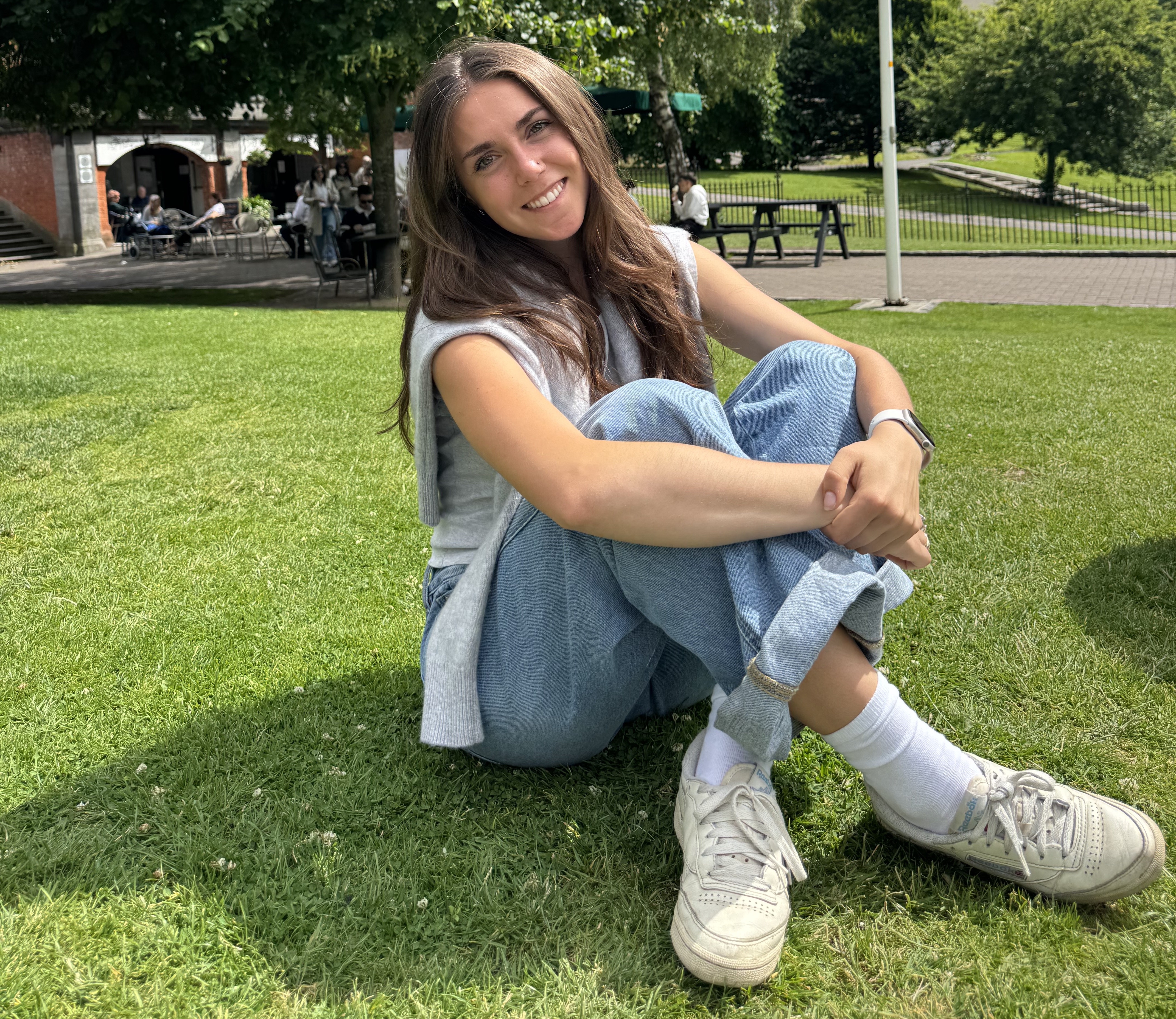 A young woman sitting on the grass outside a college building