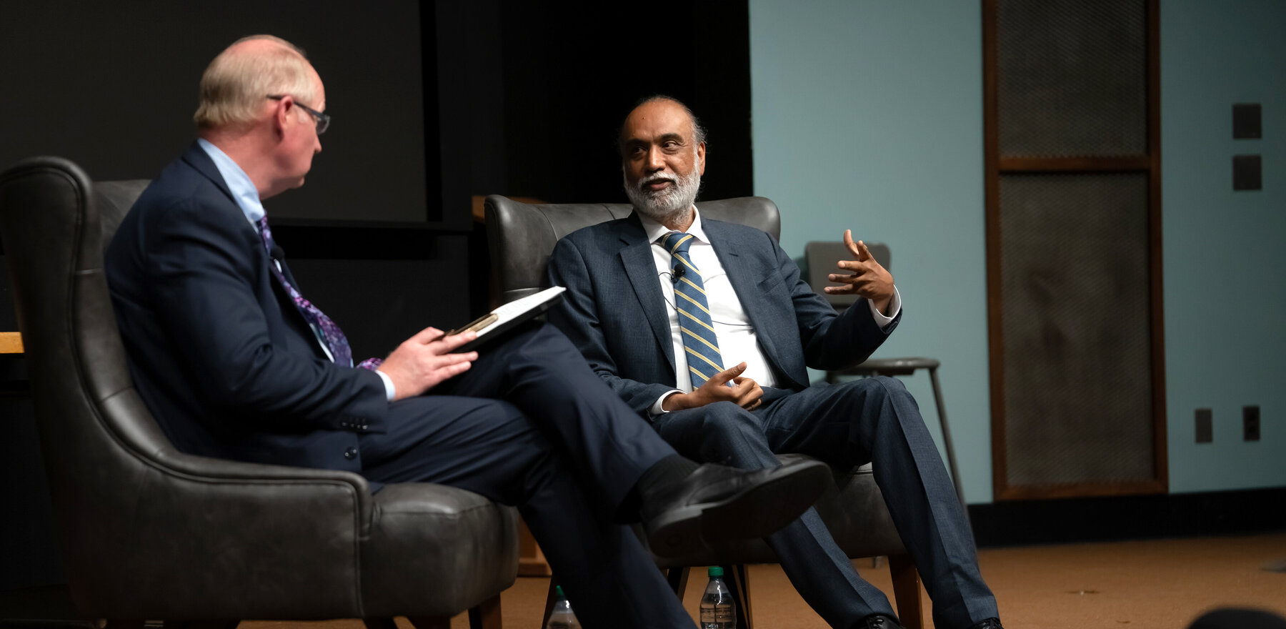 Two men sitting on tables on a stage talking to each other