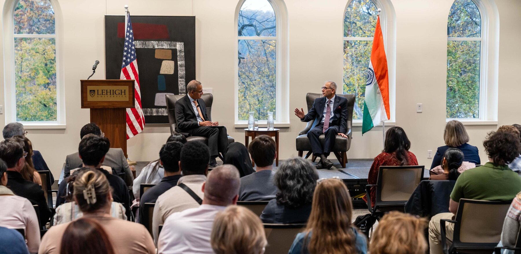Two men sitting on a stage talking in front of a crowd