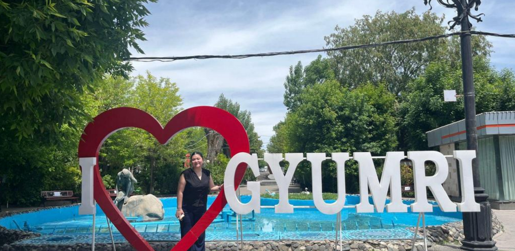 A woman standing near a big sign display that says I Heart Gyumri