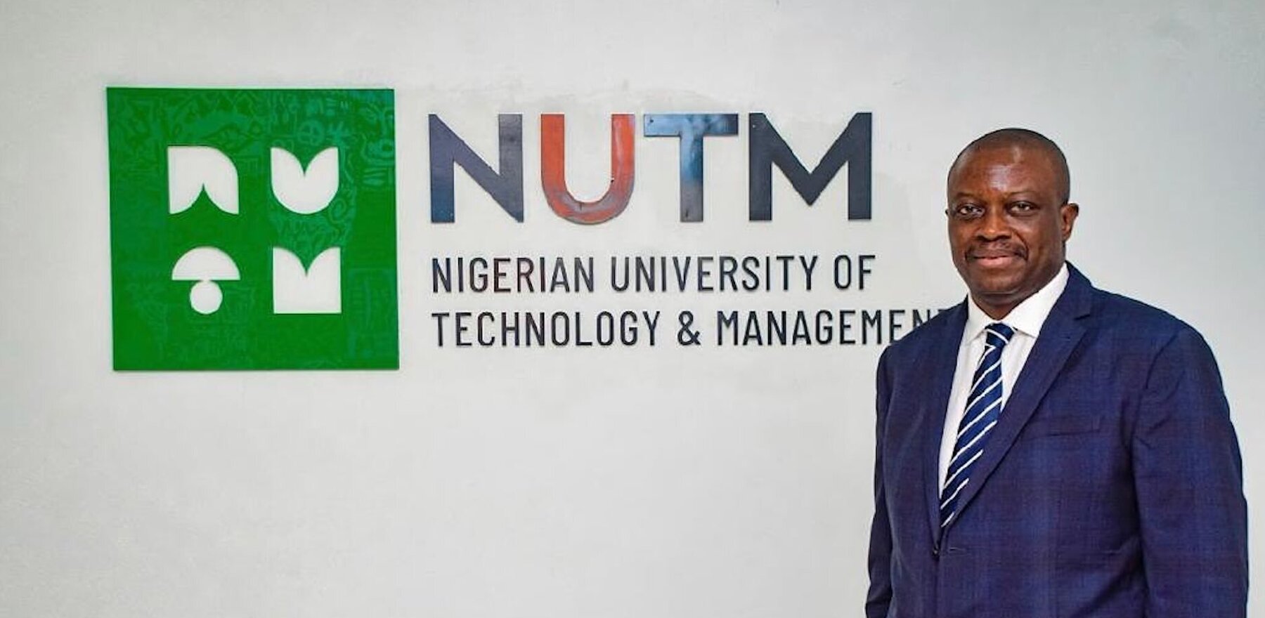 A man standing in front of the logo for the Nigerian University of Technology and Management (NUTM)