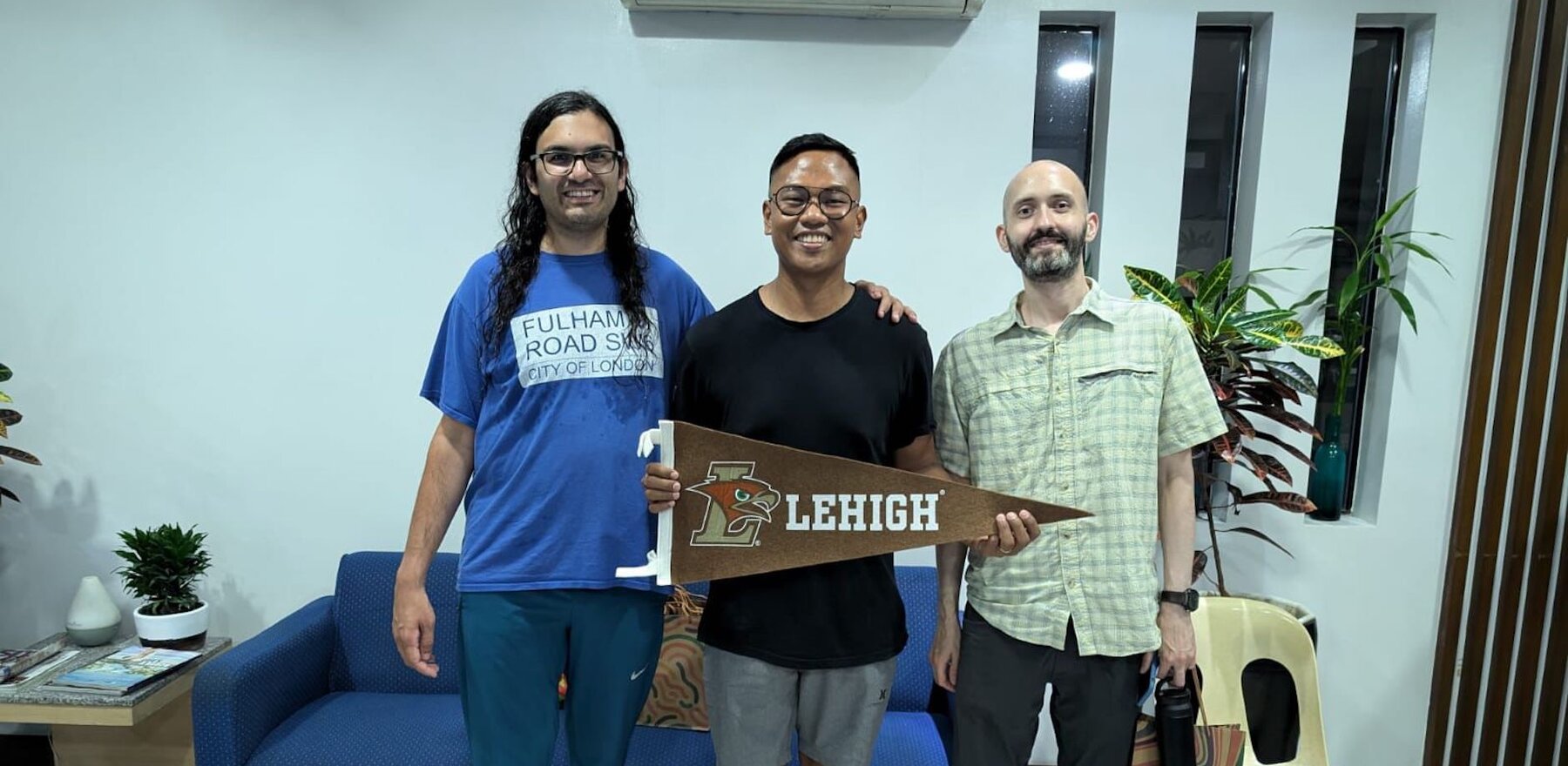 Three people smiling for the camera, with one holding a Lehigh University flag