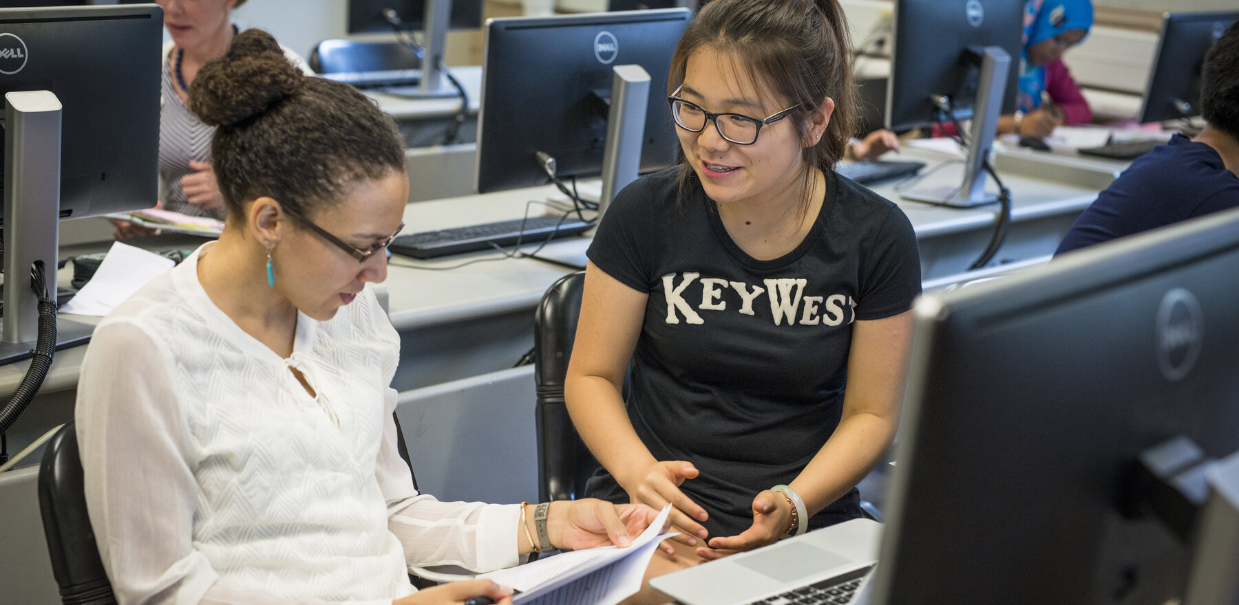 Two people discussing a paper while sitting in front of a computer