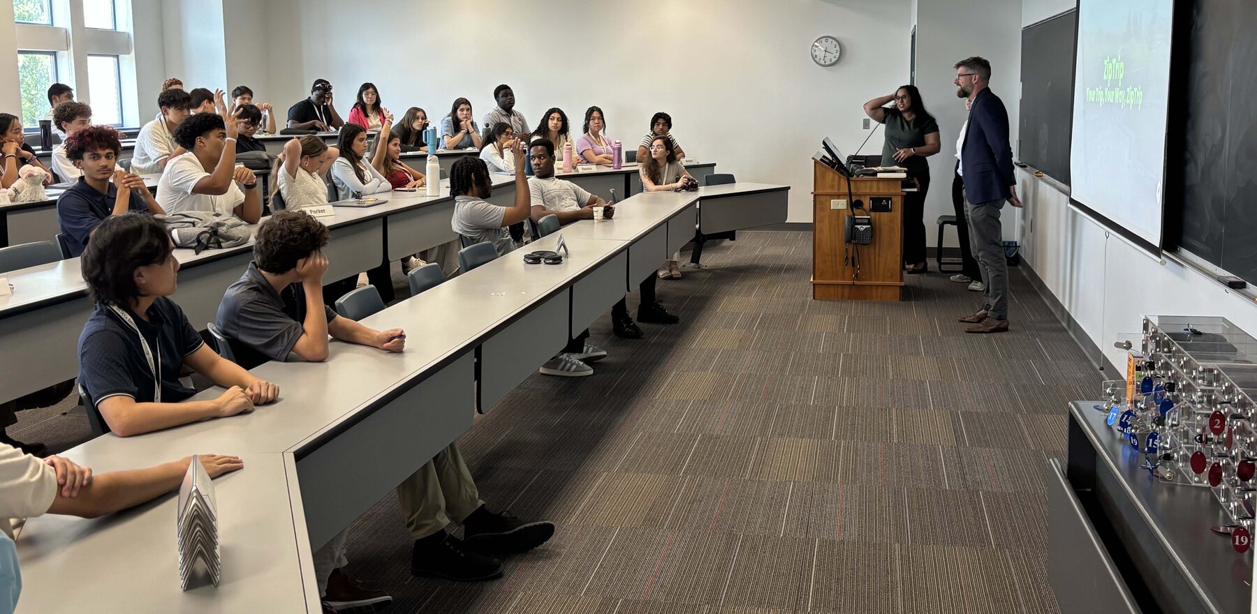 Students in a classroom listening to speakers standing by a podium