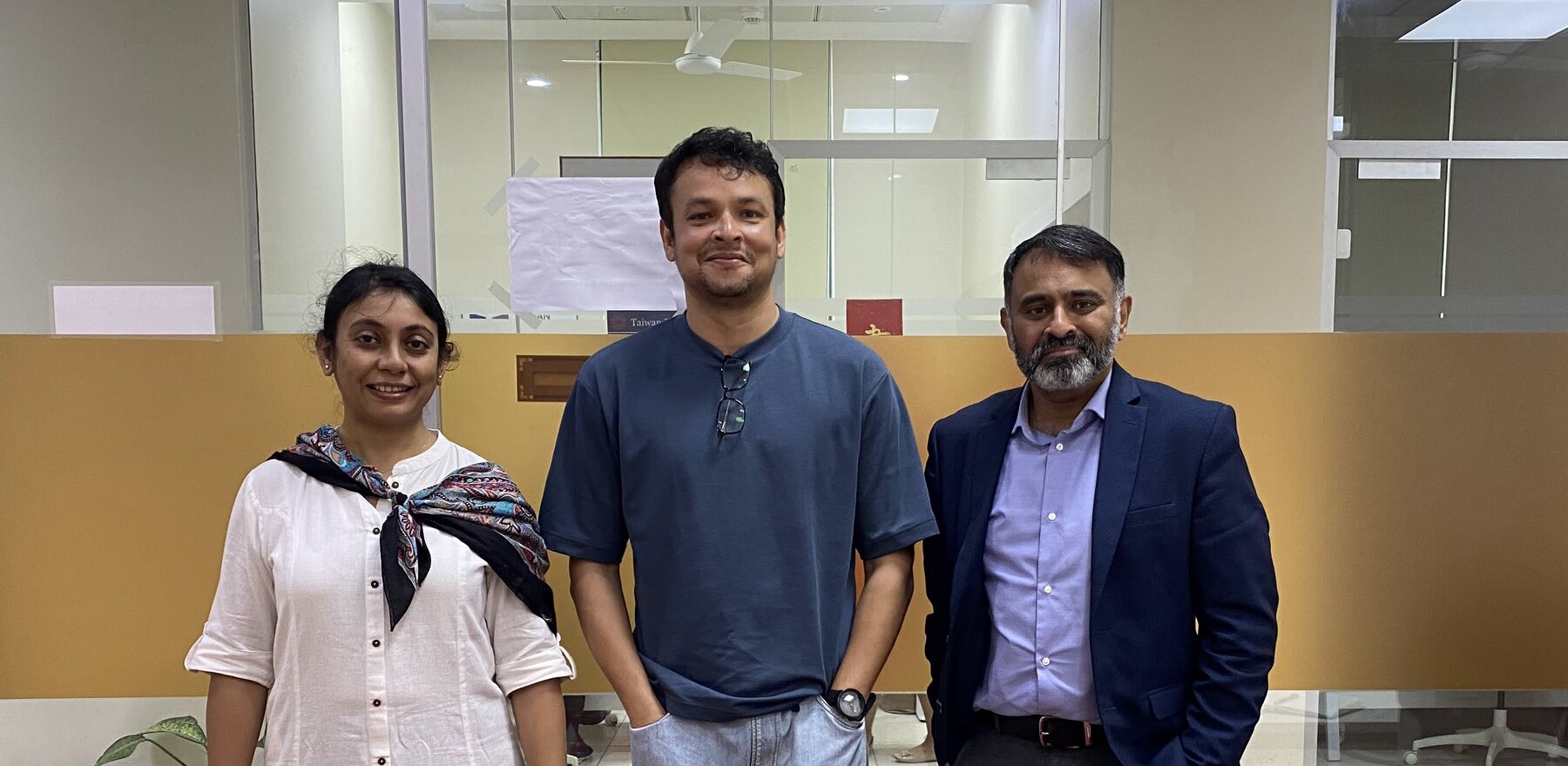 Three people in a room smiling for the camera with a glass wall behind them