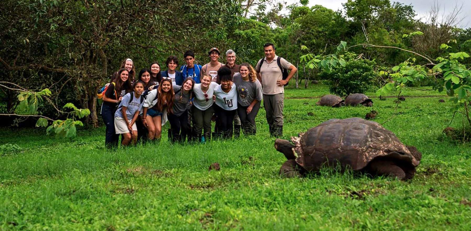 A group of students standing in a grassy field in front of a giant tortoise