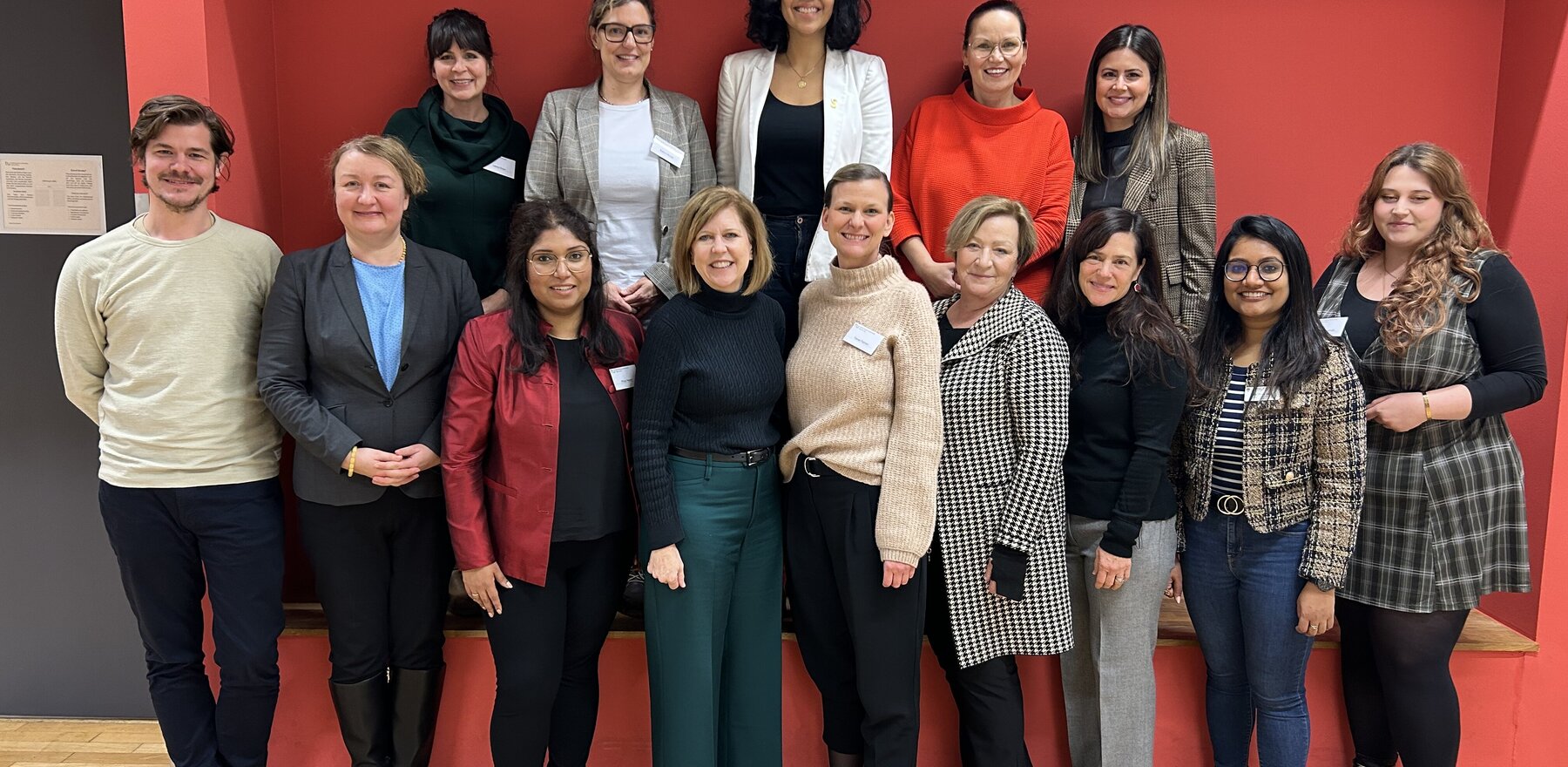 A group of people standing in front of a red wall, smiling for a photo