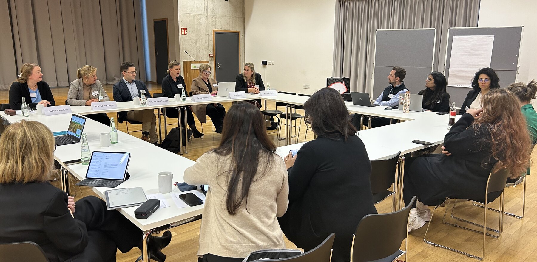 A group of people gathered around a number of tables arranged into a square