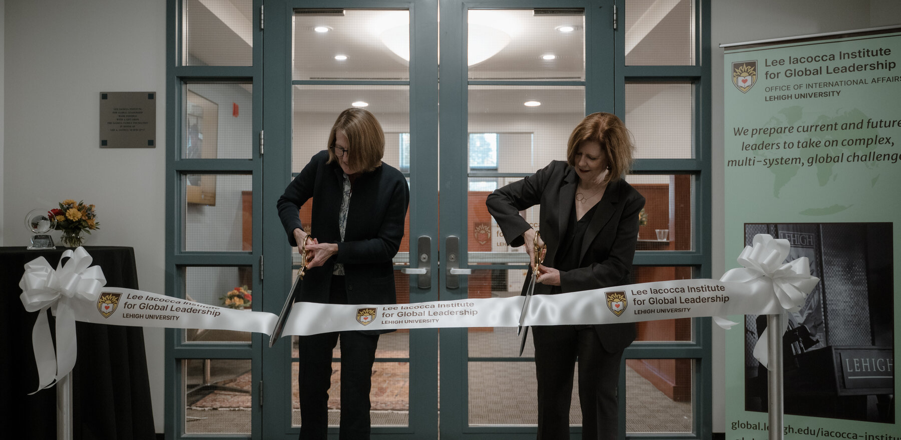 Two women cutting a ribbon at a ribbon-cutting event in an office setting