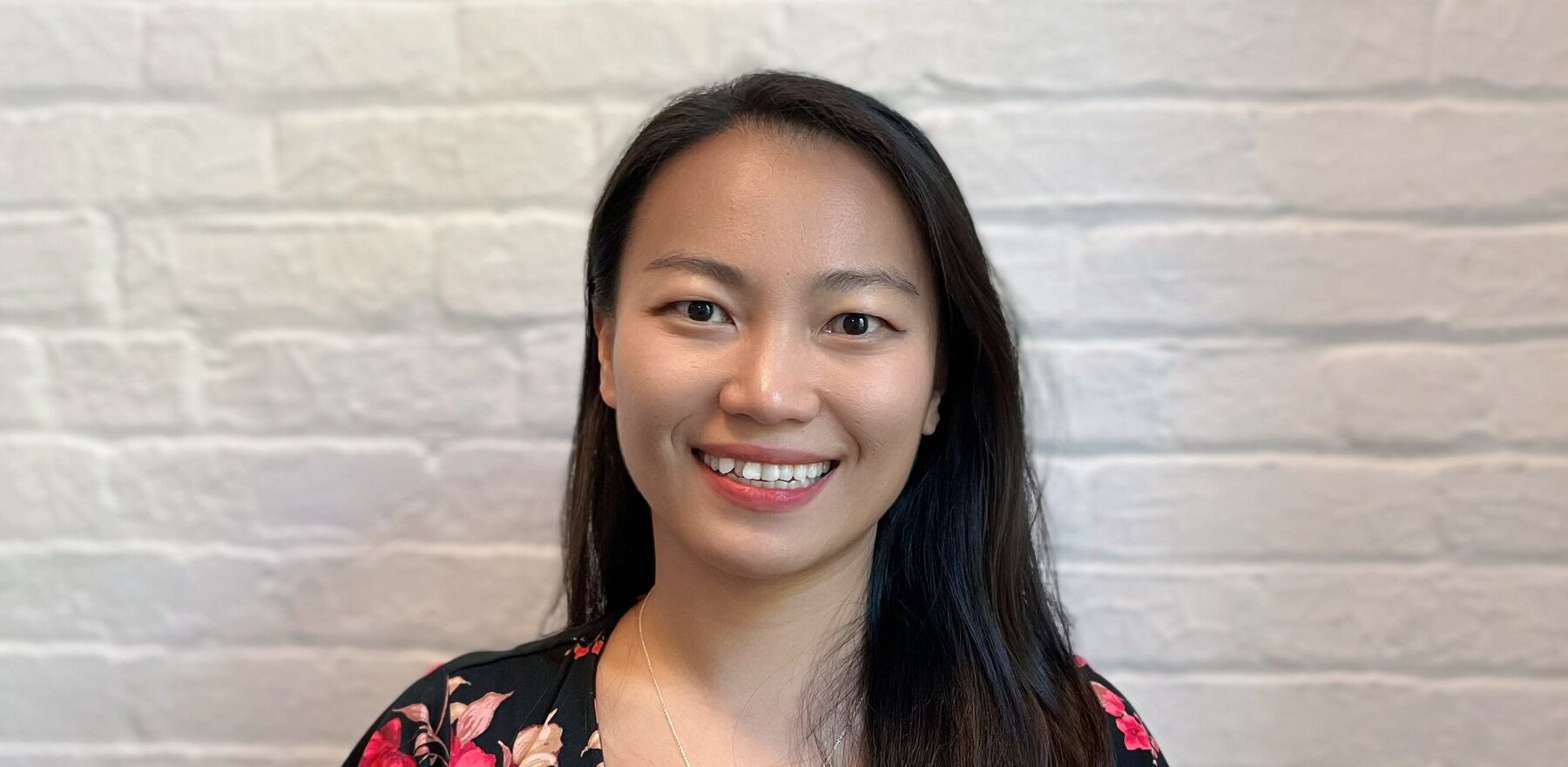 A woman smiling while standing in front of white brick