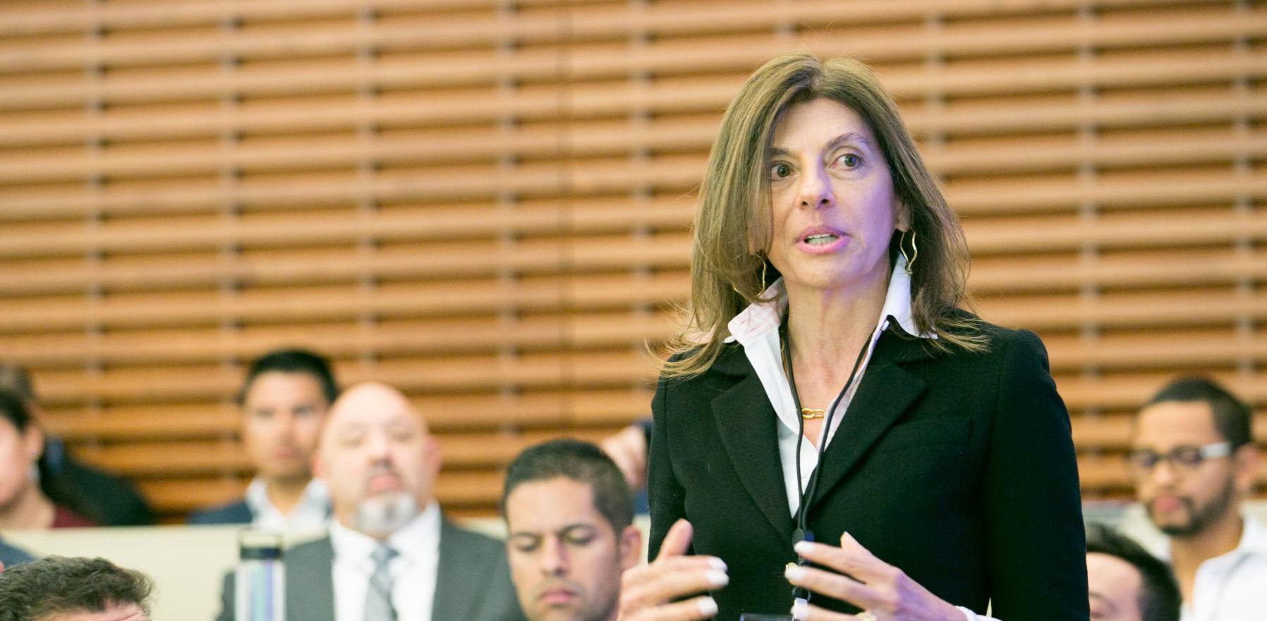 Marcela Berland speaking to a group while standing among other in an audience