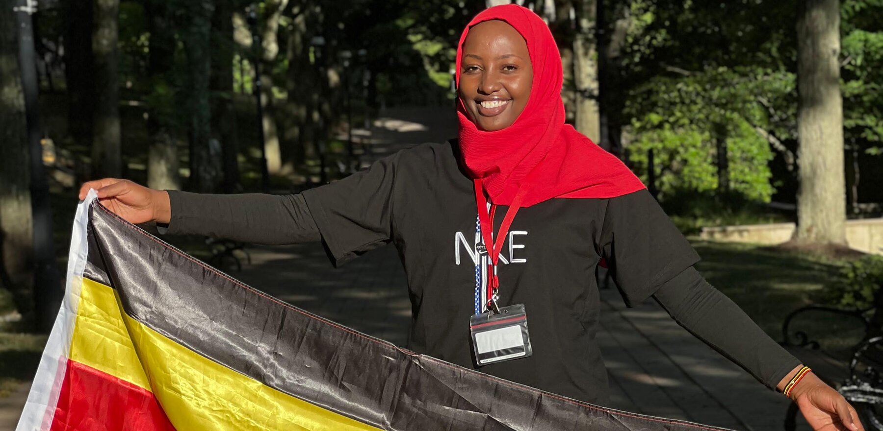 Mariam Nakigude holding a Uganda flag and smiling for the camera