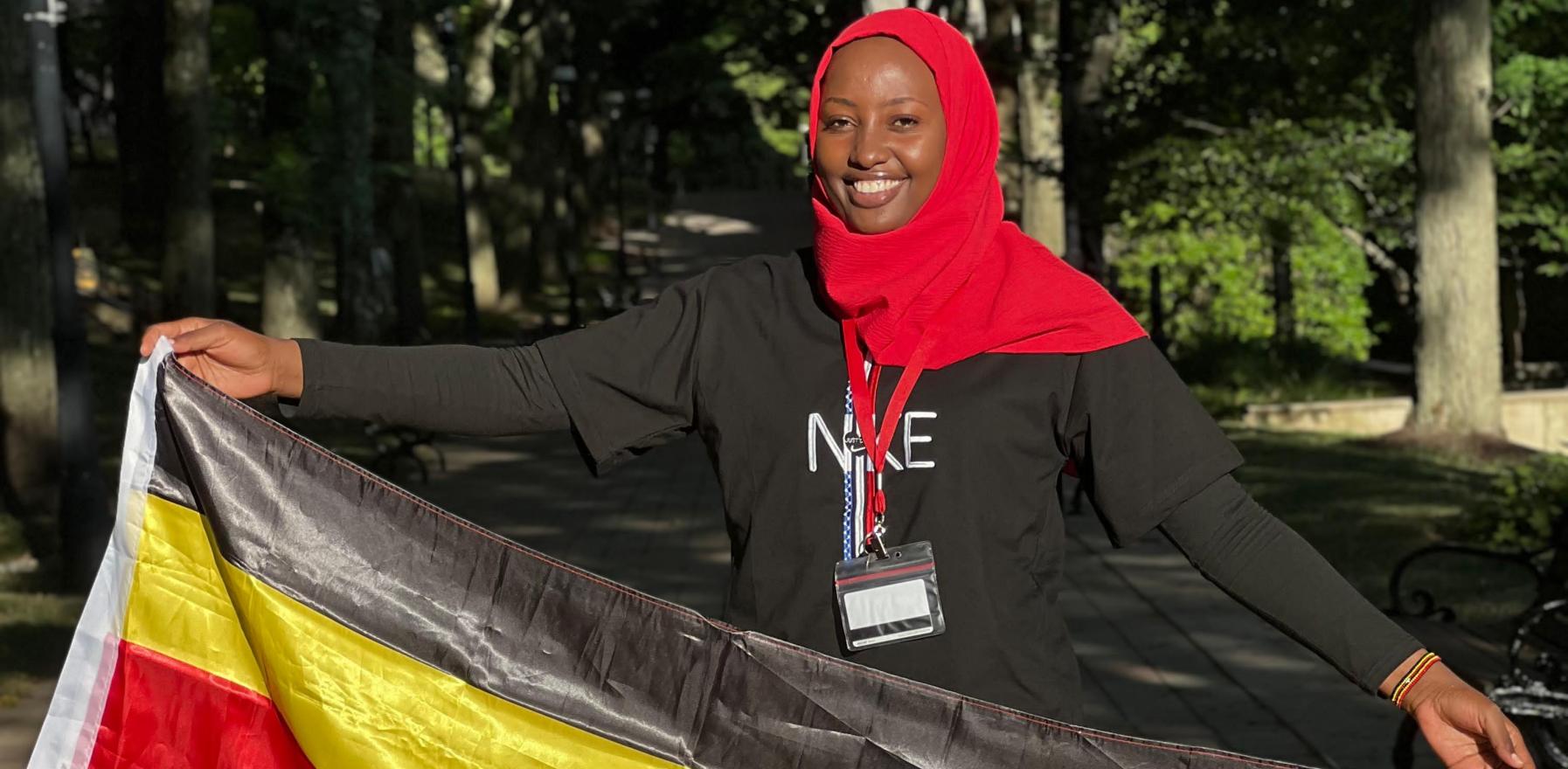 Mariam Nakigude holding a Uganda flag and smiling for the camera