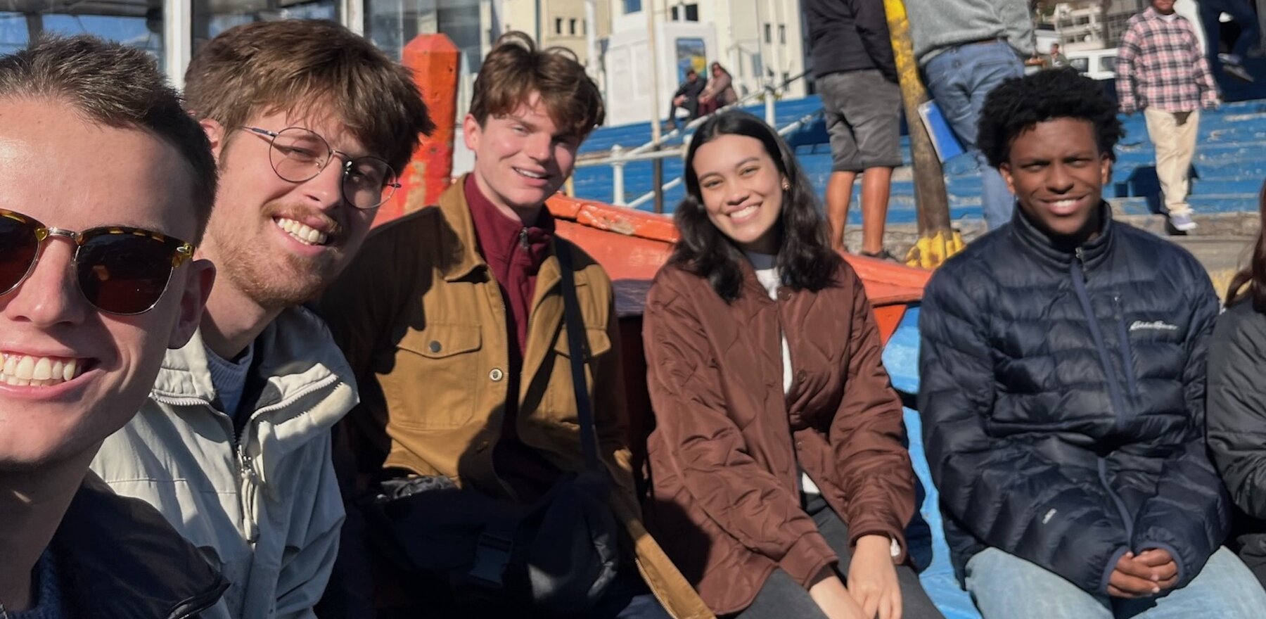 A group of five young people sit together and smile at the camera