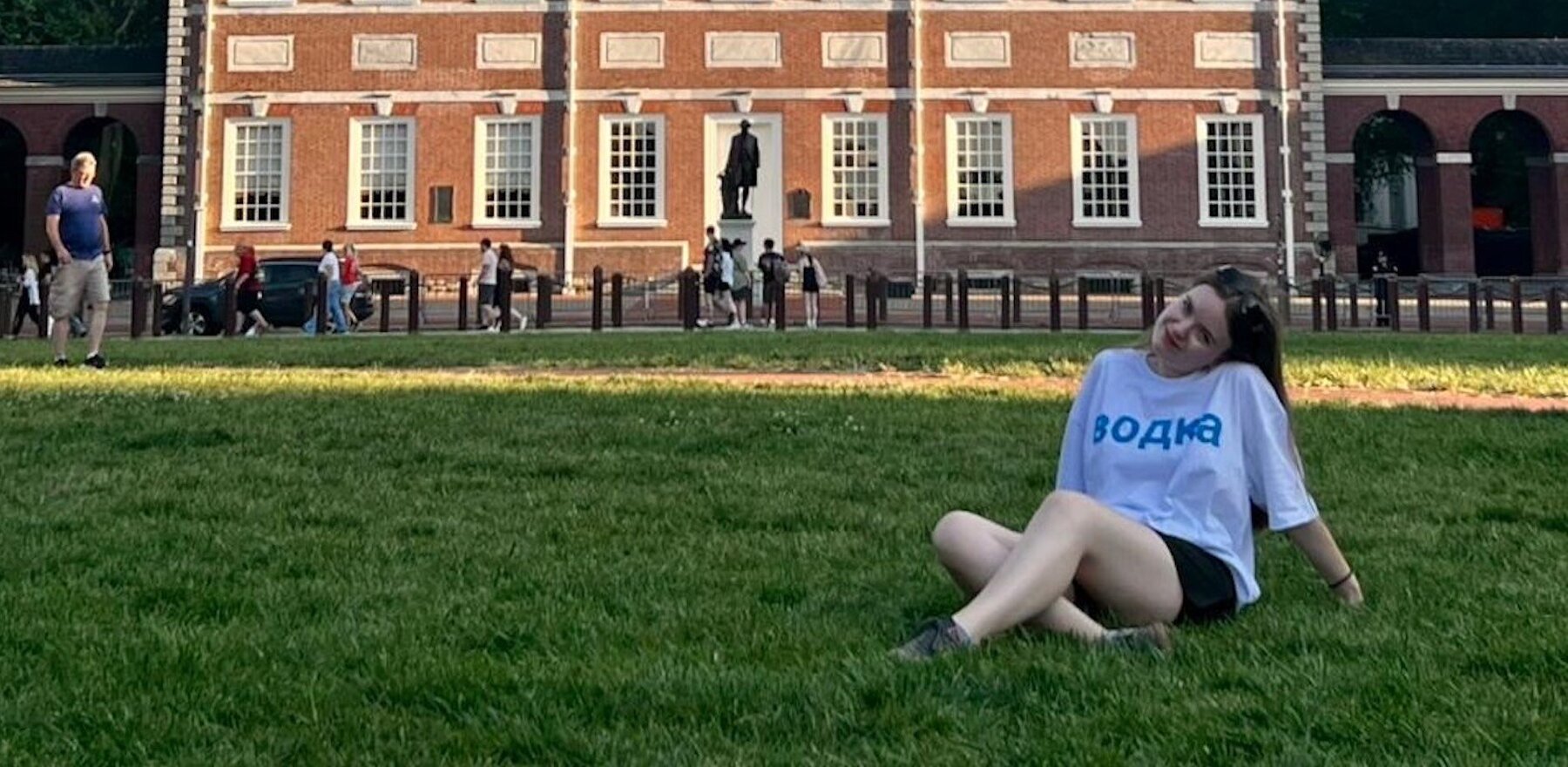 A young woman lays on the grass in front of a university building