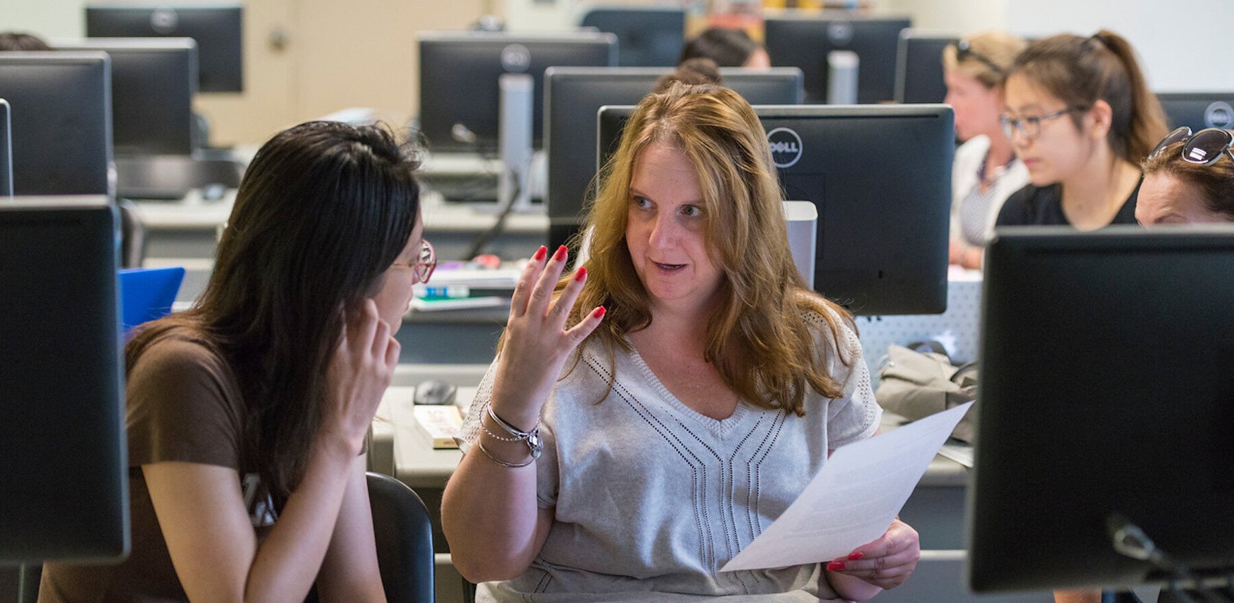 A teacher providing instruction to a student as they sit in front of a computer
