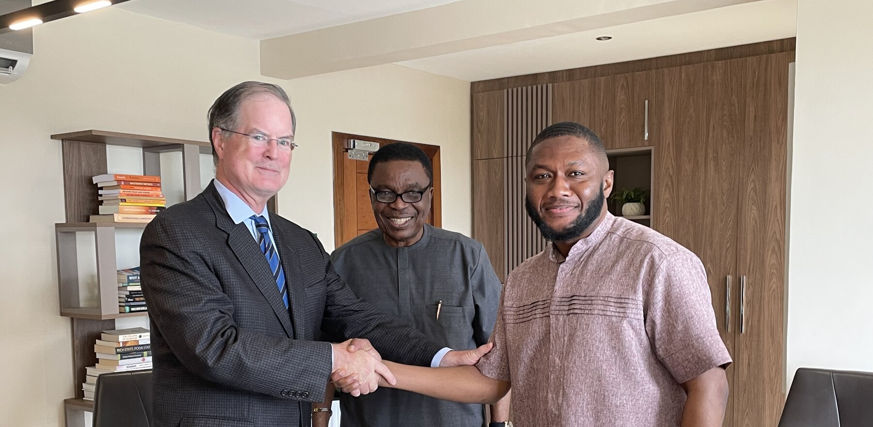 Two men shaking hand and smiling for the camera as another smiling man stands behind them