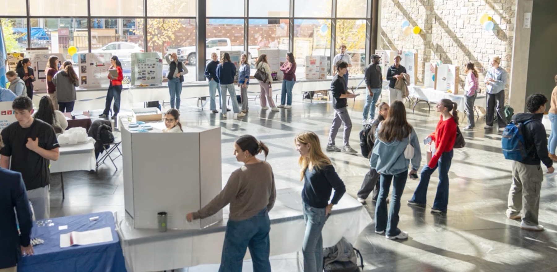 A group of people gathered in a lobby with information tables scattered throughout the room