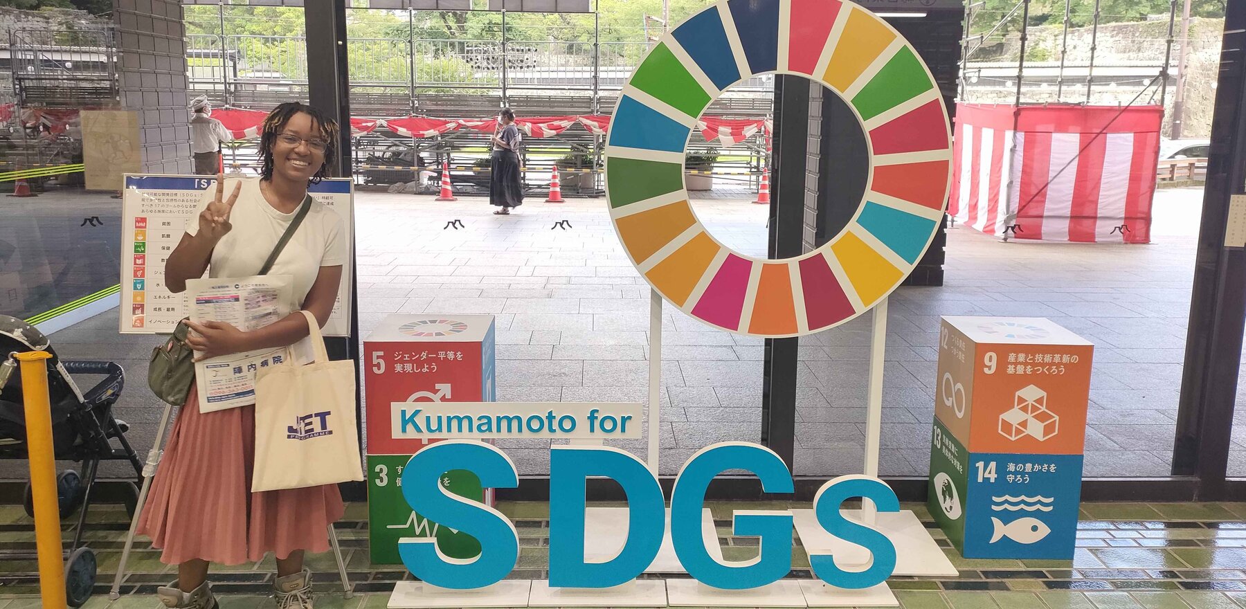 Zena Meighan standing in front of a display that says Kumamoto for SDGs