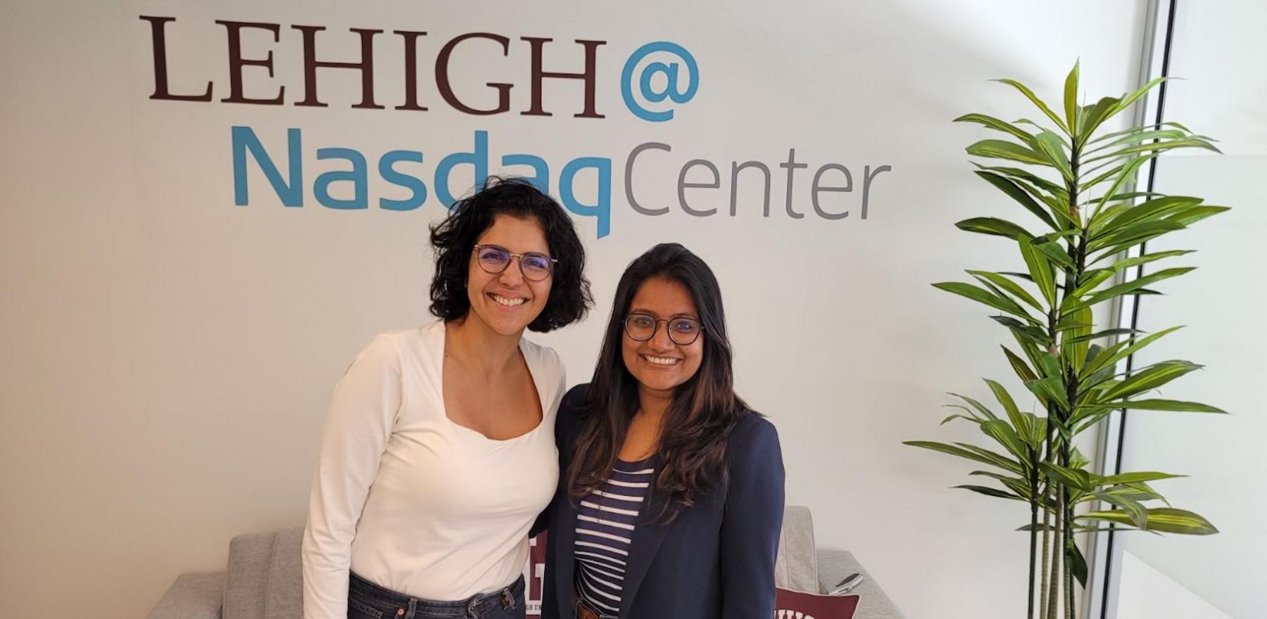 Two women stand in front of a Lehigh@NasdaqCenter logo